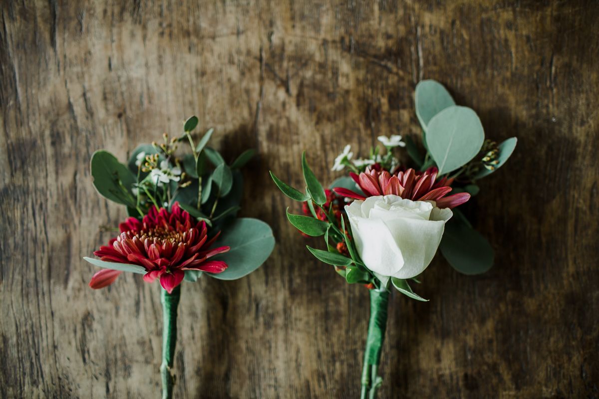 Two elegant wedding boutonnieres with red and white flowers against rustic wooden background.