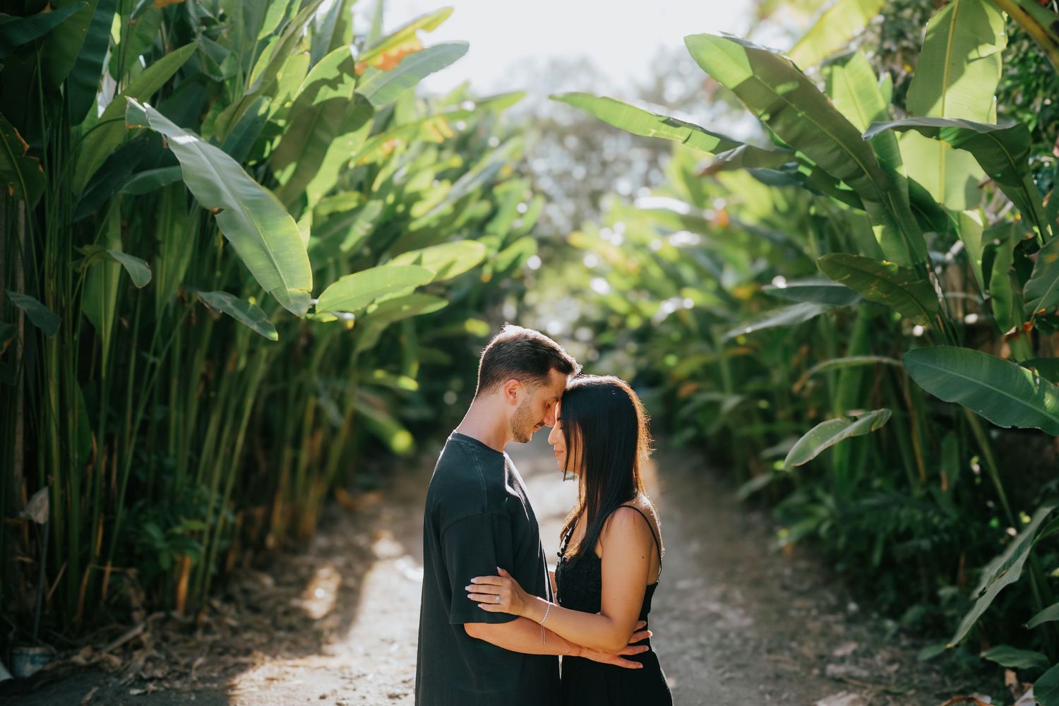 Intimate couple embracing in tropical garden pathway surrounded by lush green plants.