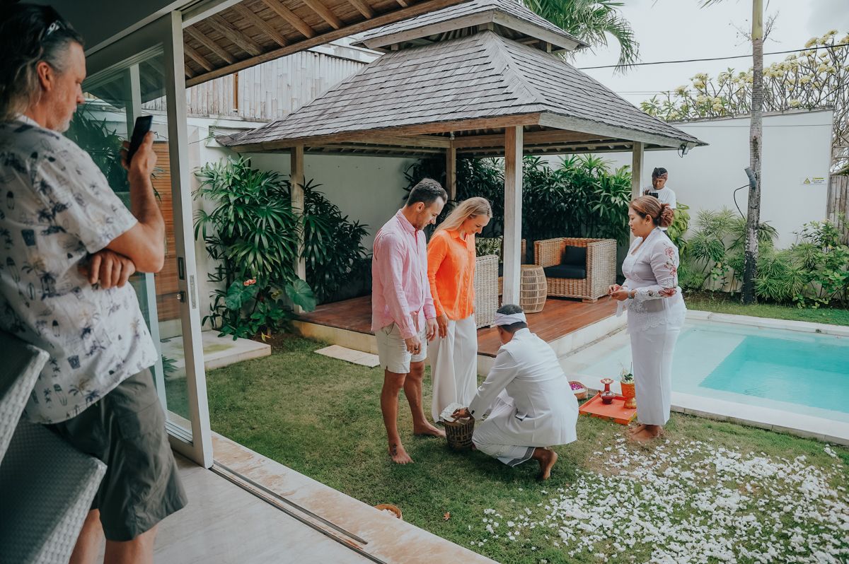 Outdoor celebration scene with people in light colored clothing gathered near a swimming pool.