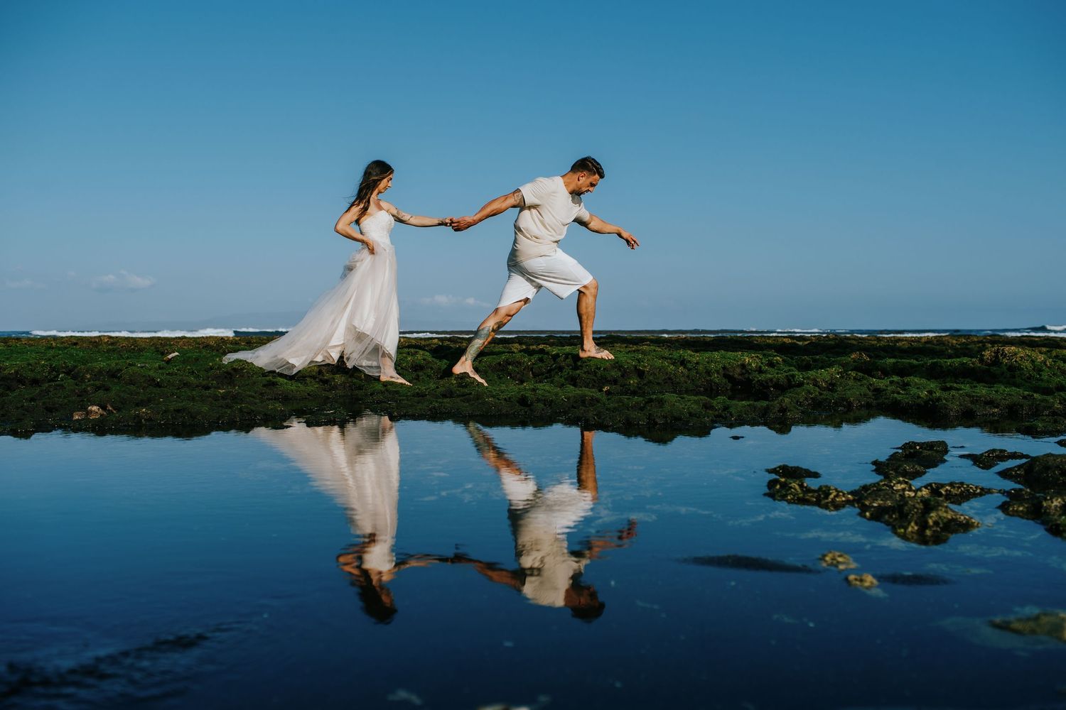 Couple dancing and playing in shallow coastal waters with reflections.
