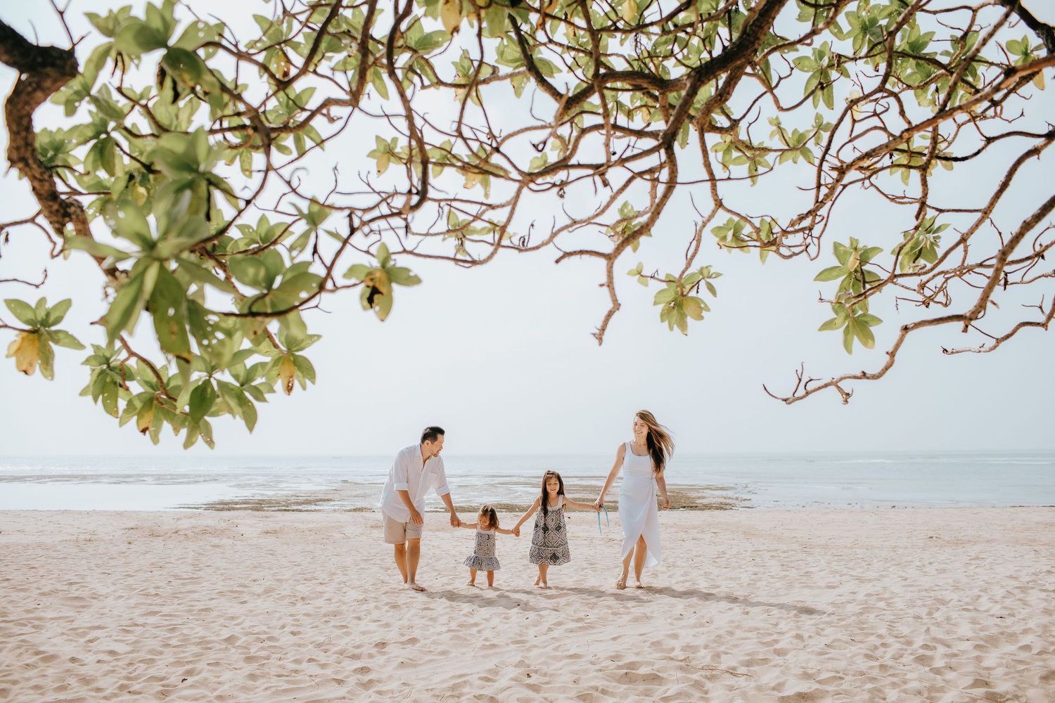 Family moment captured under blooming tree branches on sandy beach.