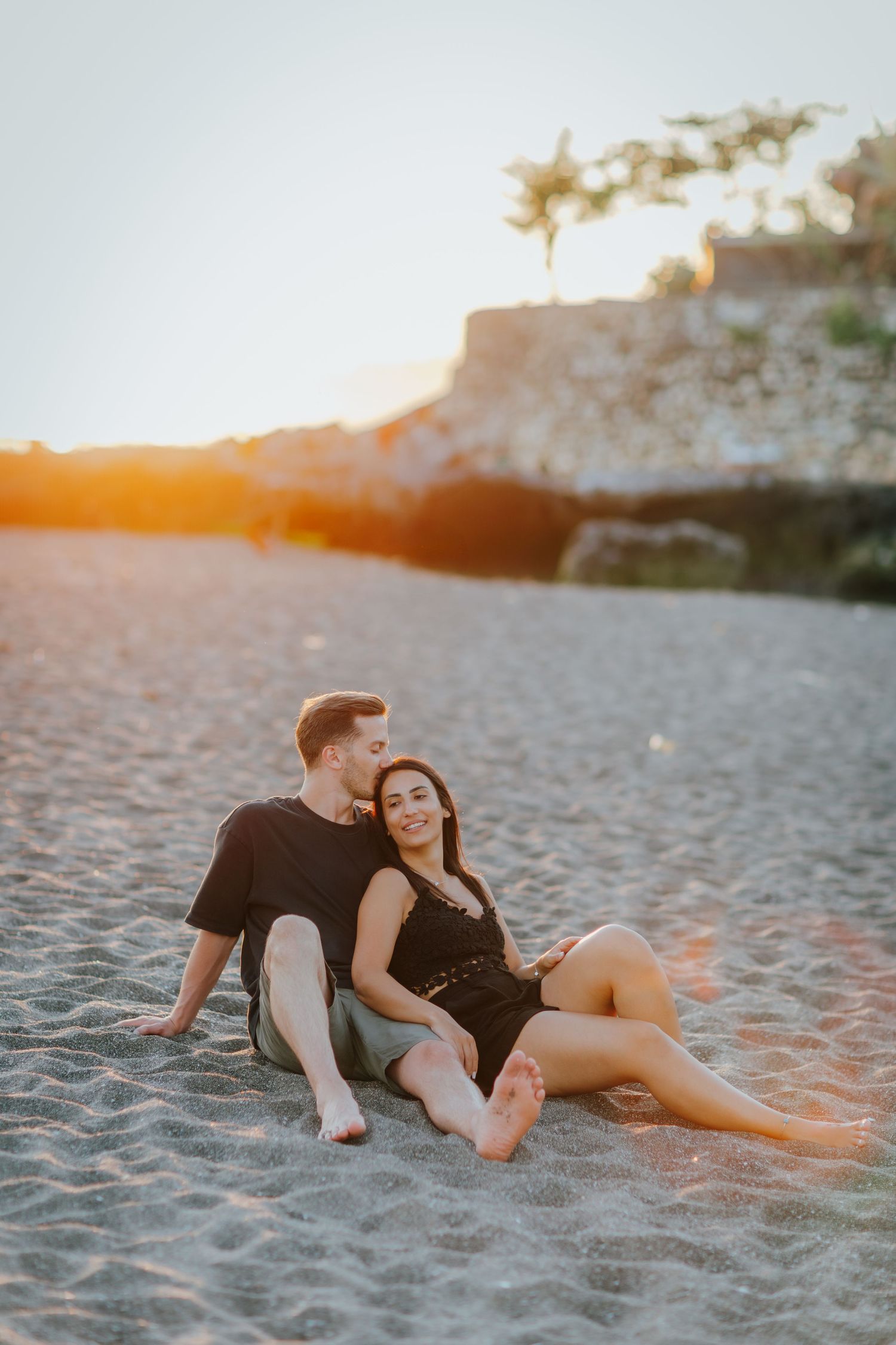 Couple lying together intimately on sandy beach during warm sunset.