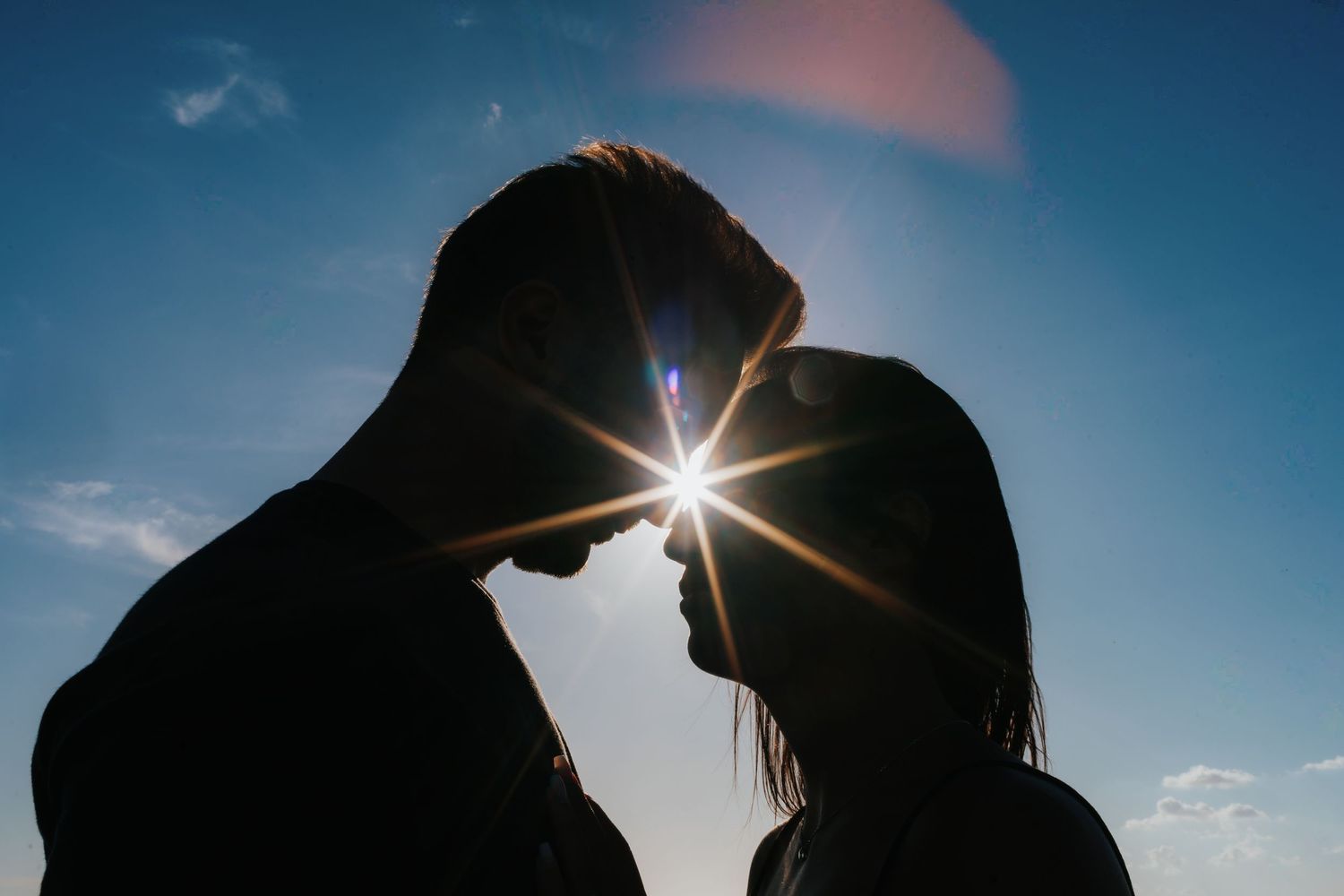 Dramatic silhouettes against vibrant blue sky with sun flare creating romantic atmosphere.