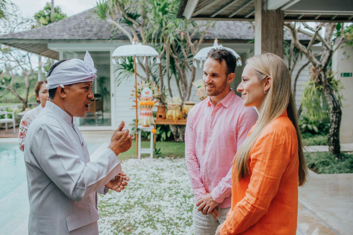 Group of people in pastel and bright orange outfits gathering outdoors under covered area.