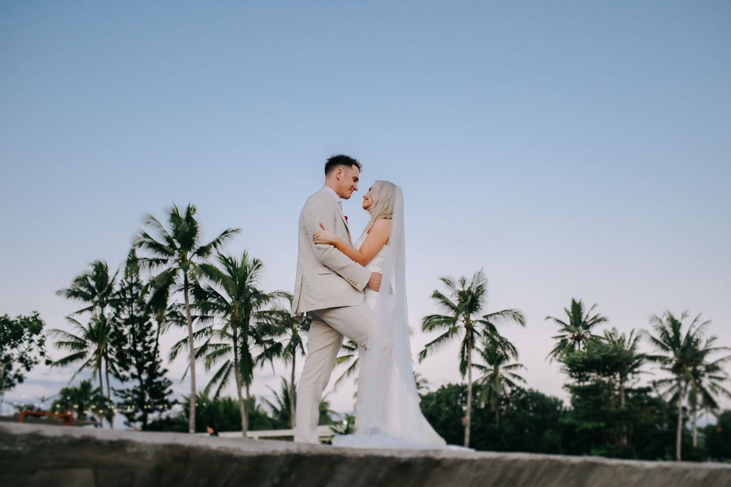 Romantic beachside wedding photos with palm trees and ocean backdrop at sunset.