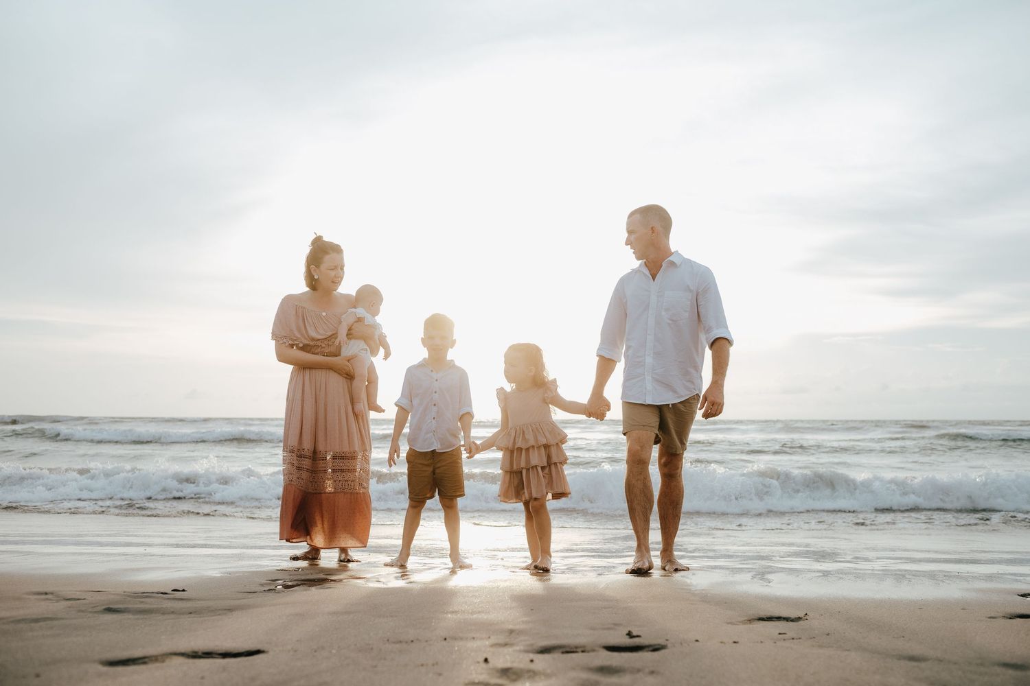Family silhouetted against sunset on beach holding hands.