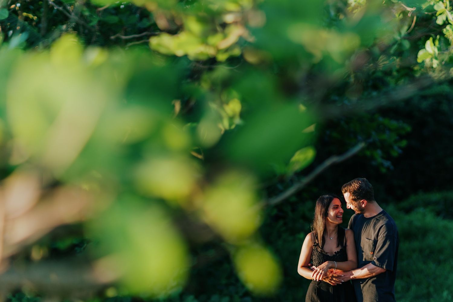 Romantic couple sharing intimate moments through green foliage in a tropical setting.
