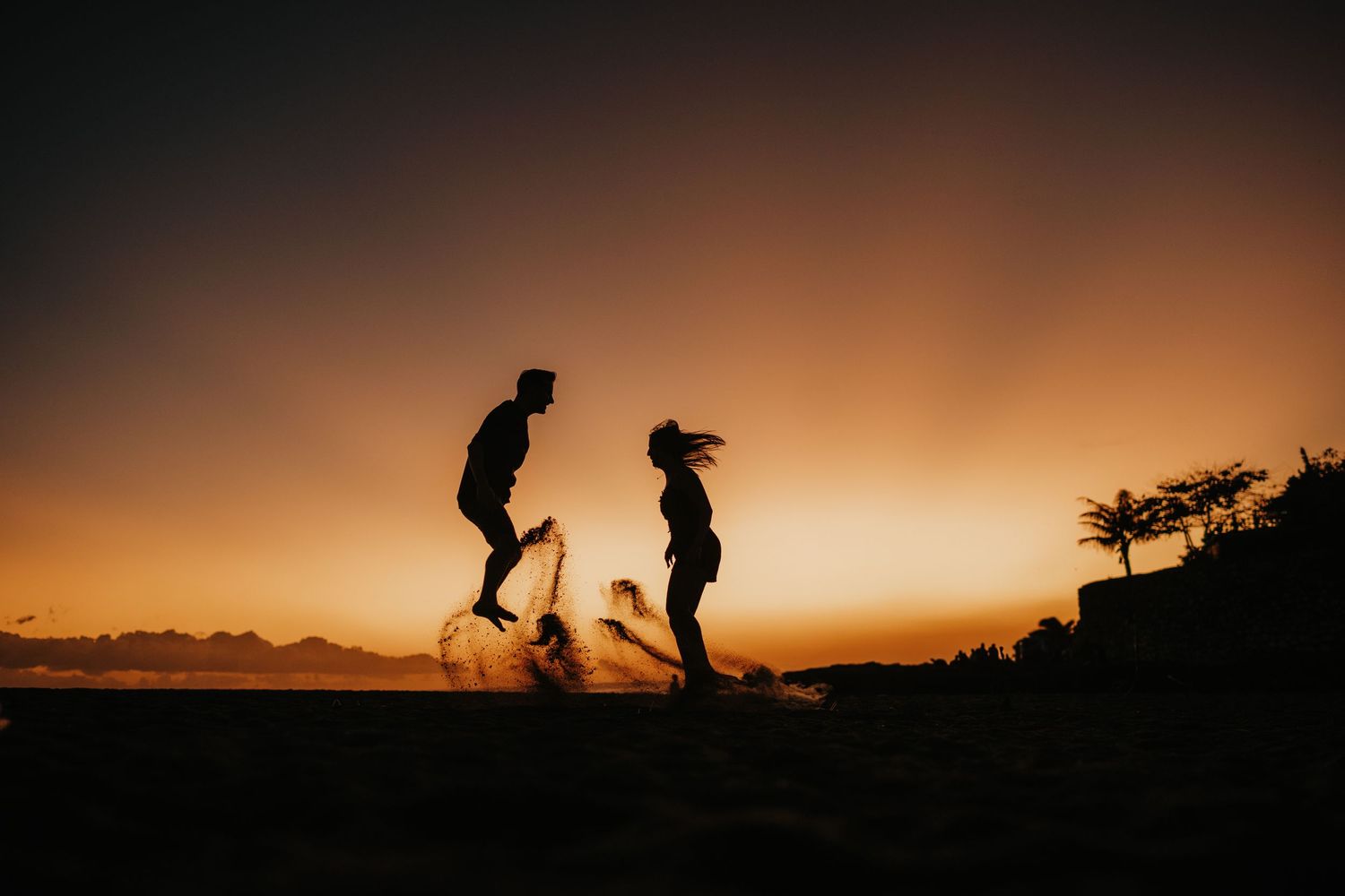 Playful silhouettes dancing on hilltop during vibrant sunset.