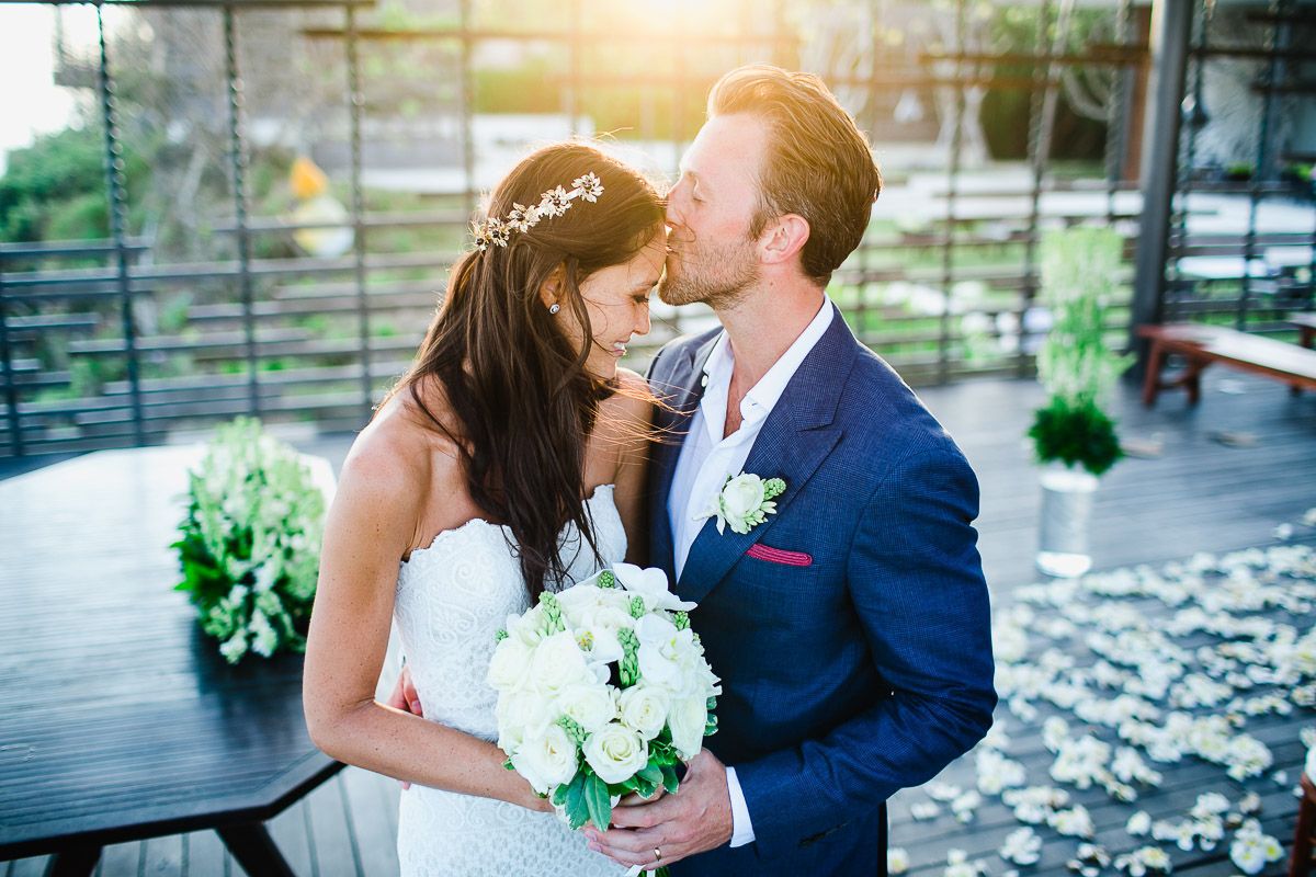 Romantic wedding couple sharing a tender moment on a decorated outdoor terrace.