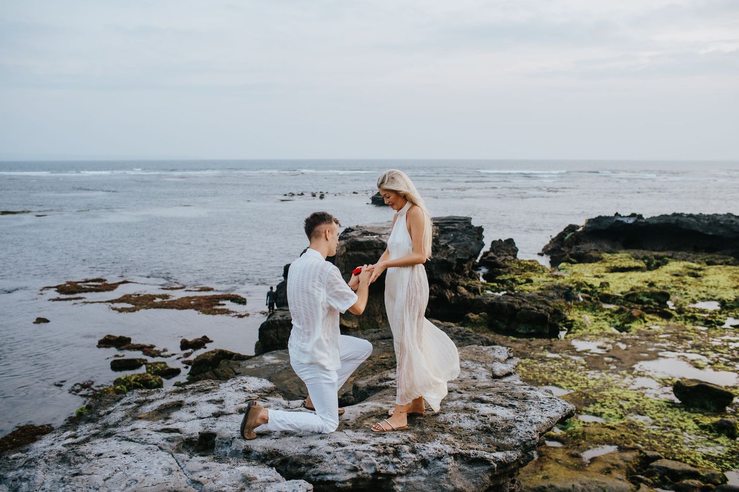 Couple dancing together on rocky ocean shore during sunset.