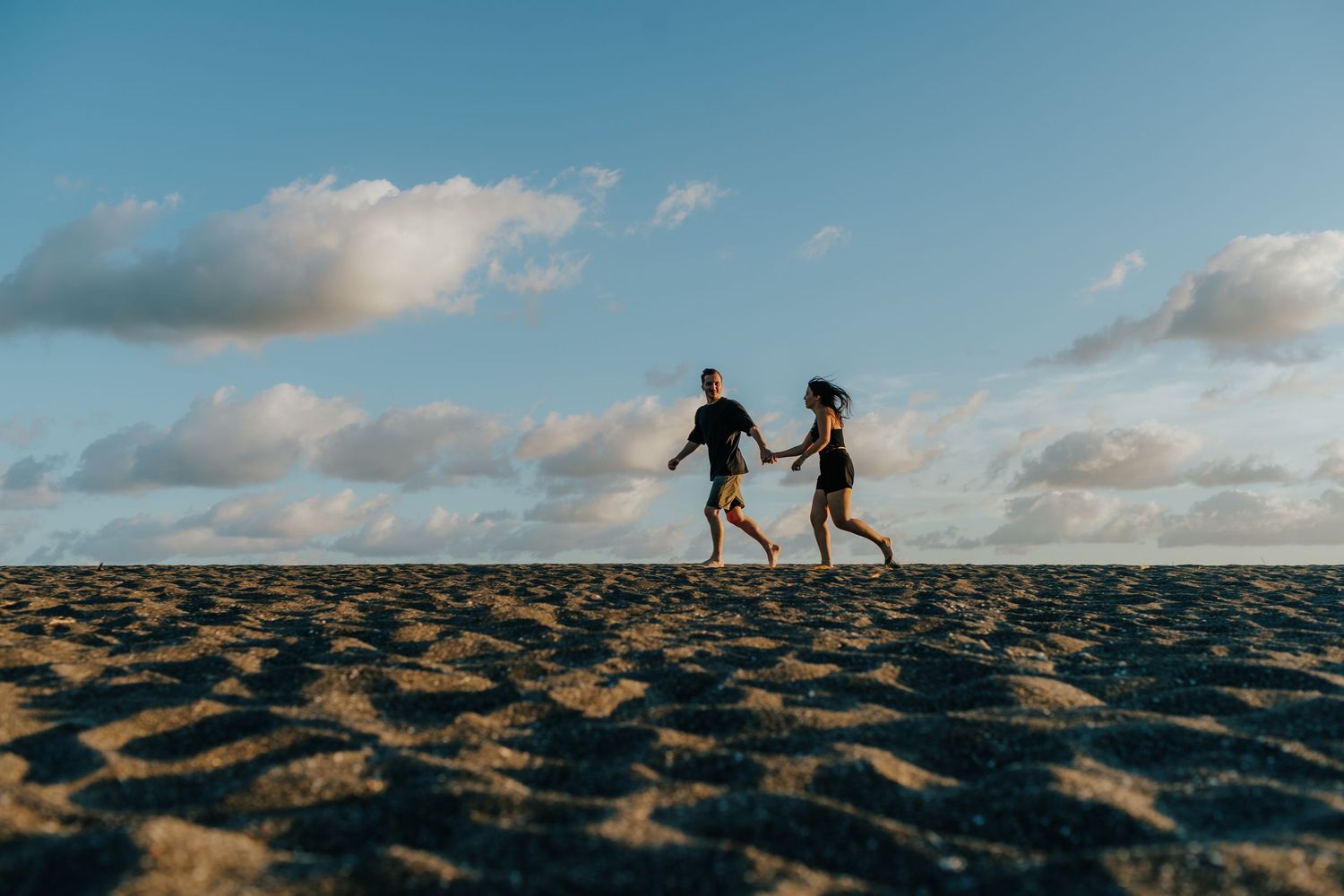 Silhouettes of two people walking on black sand beach during golden hour.