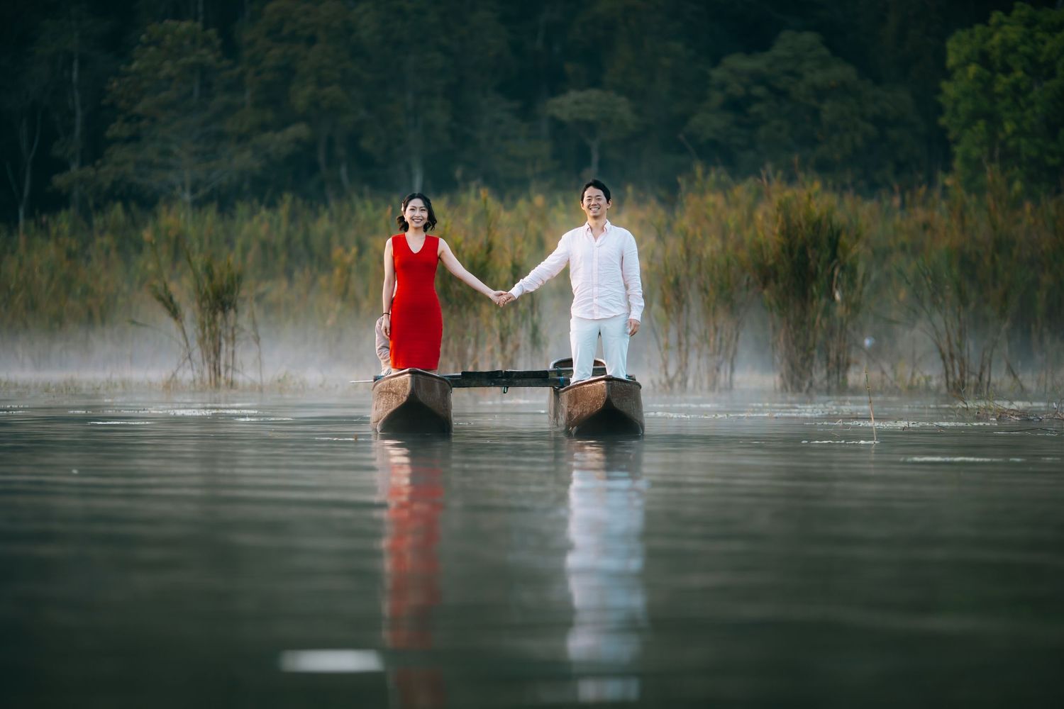 Moody photos of figures in red and white clothing reflected in still misty water at dawn.