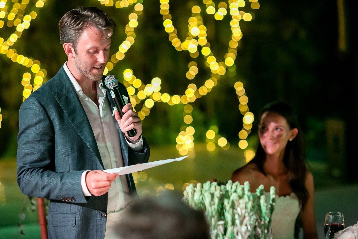 Evening wedding reception speeches illuminated by warm string lights and bokeh effects.