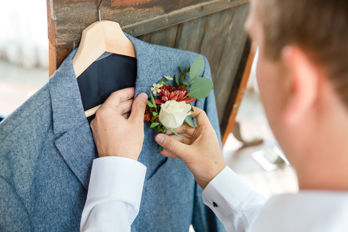 Close-up of hands pinning a white and red boutonnière to a blue suit jacket.