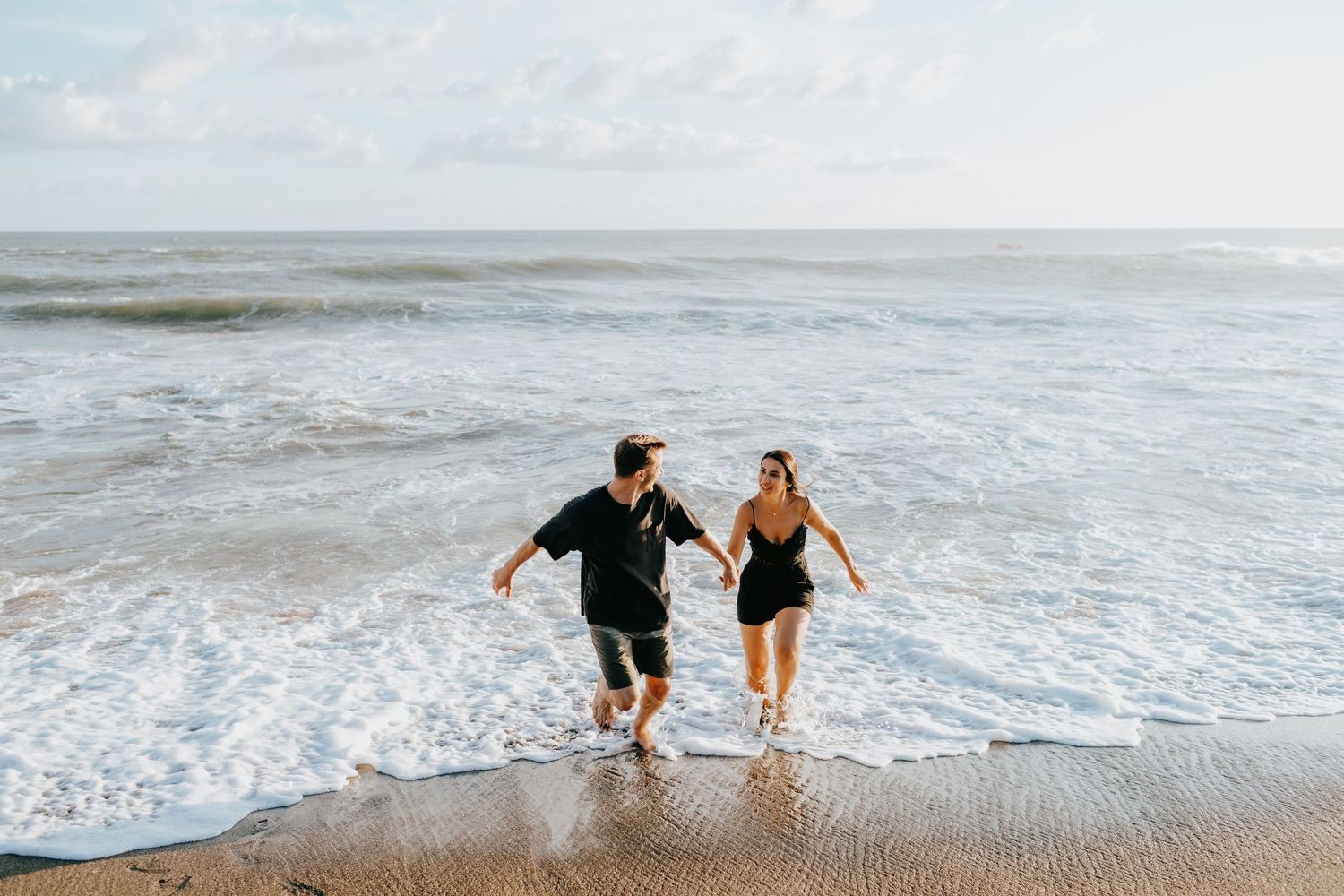 Couple splashing and playing in the ocean waves during a beach photoshoot.