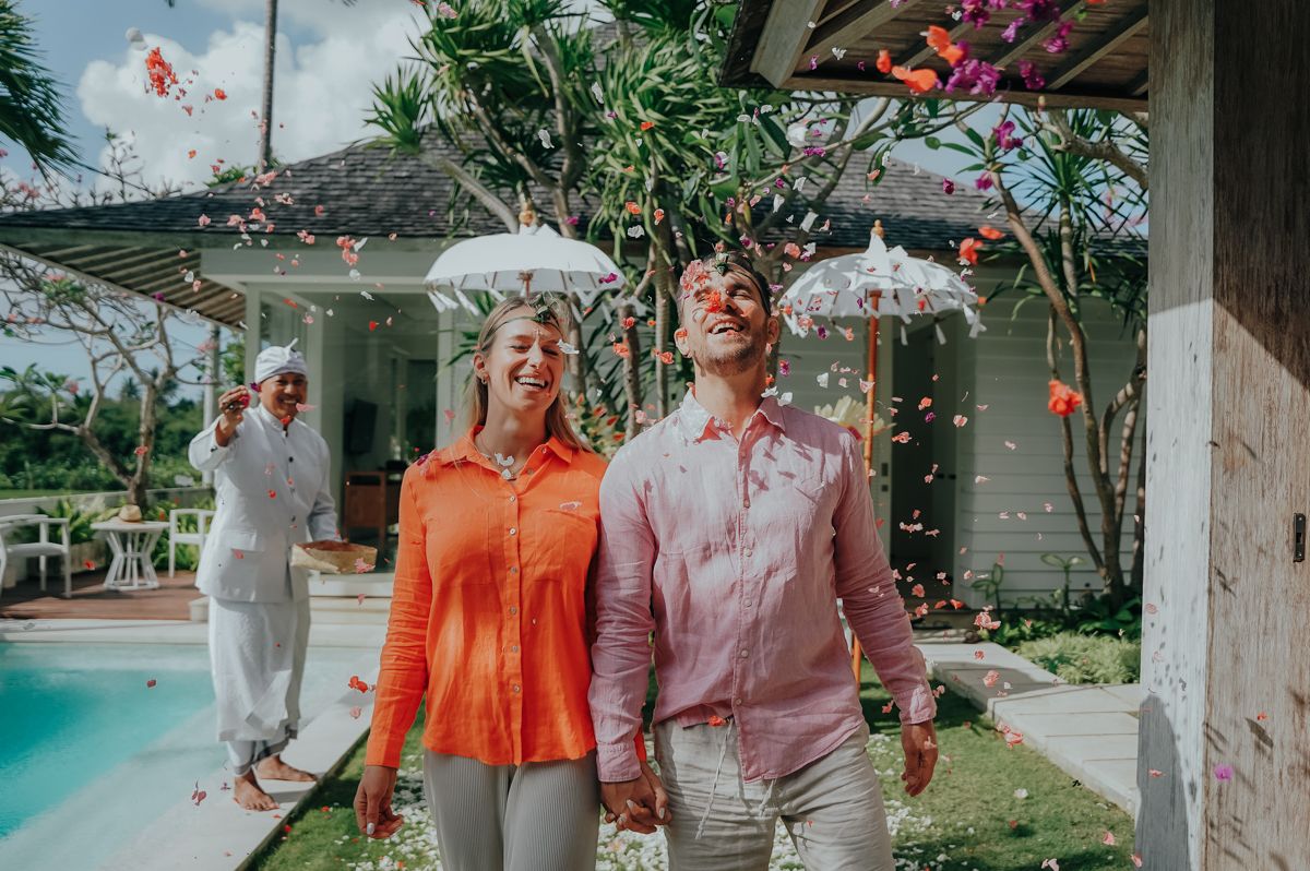 Garden party scene with guests in orange and white outfits walking under decorative umbrellas.