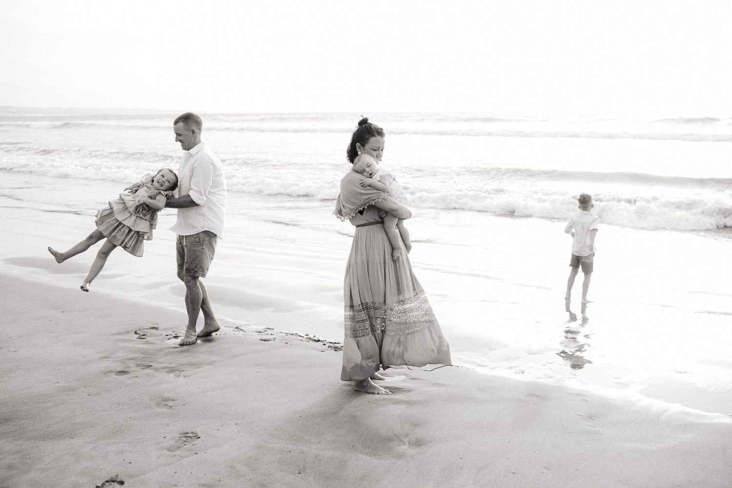 A joyful black and white photo of a family playing together on a beach at sunset.