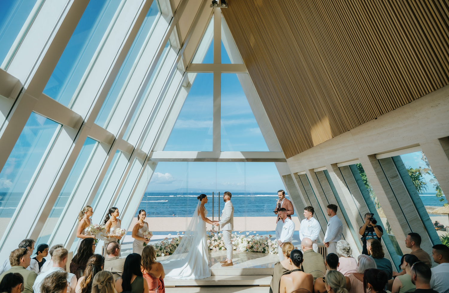 Elegant beachfront wedding ceremony in a stunning chapel with floor-to-ceiling windows overlooking the ocean.