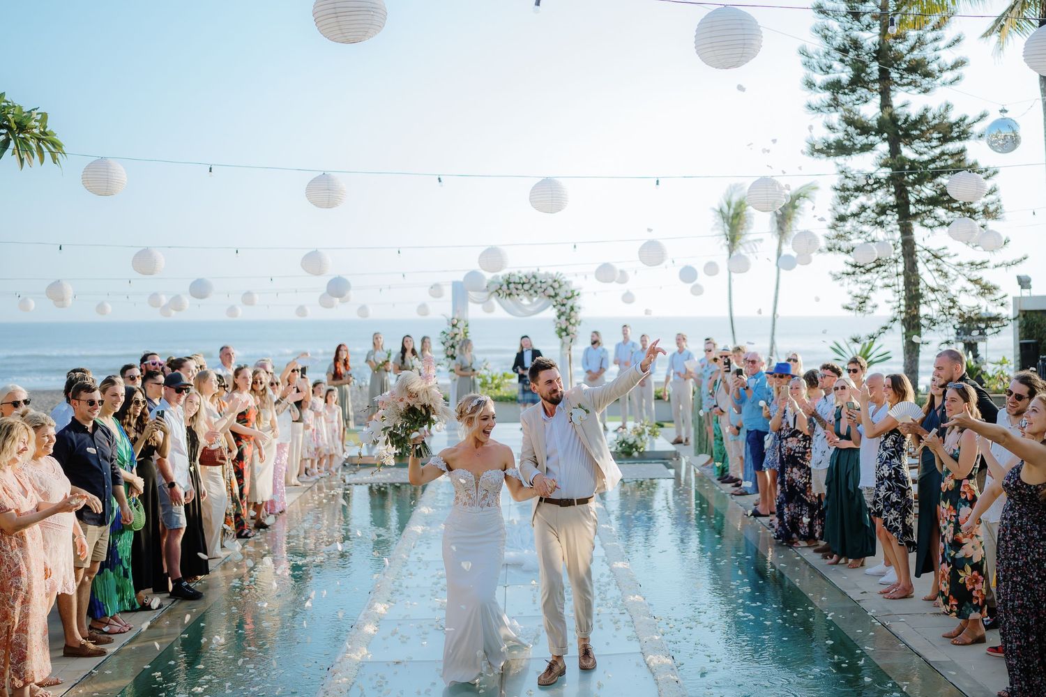 Outdoor wedding ceremony by the ocean with guests gathered around a reflective pool.