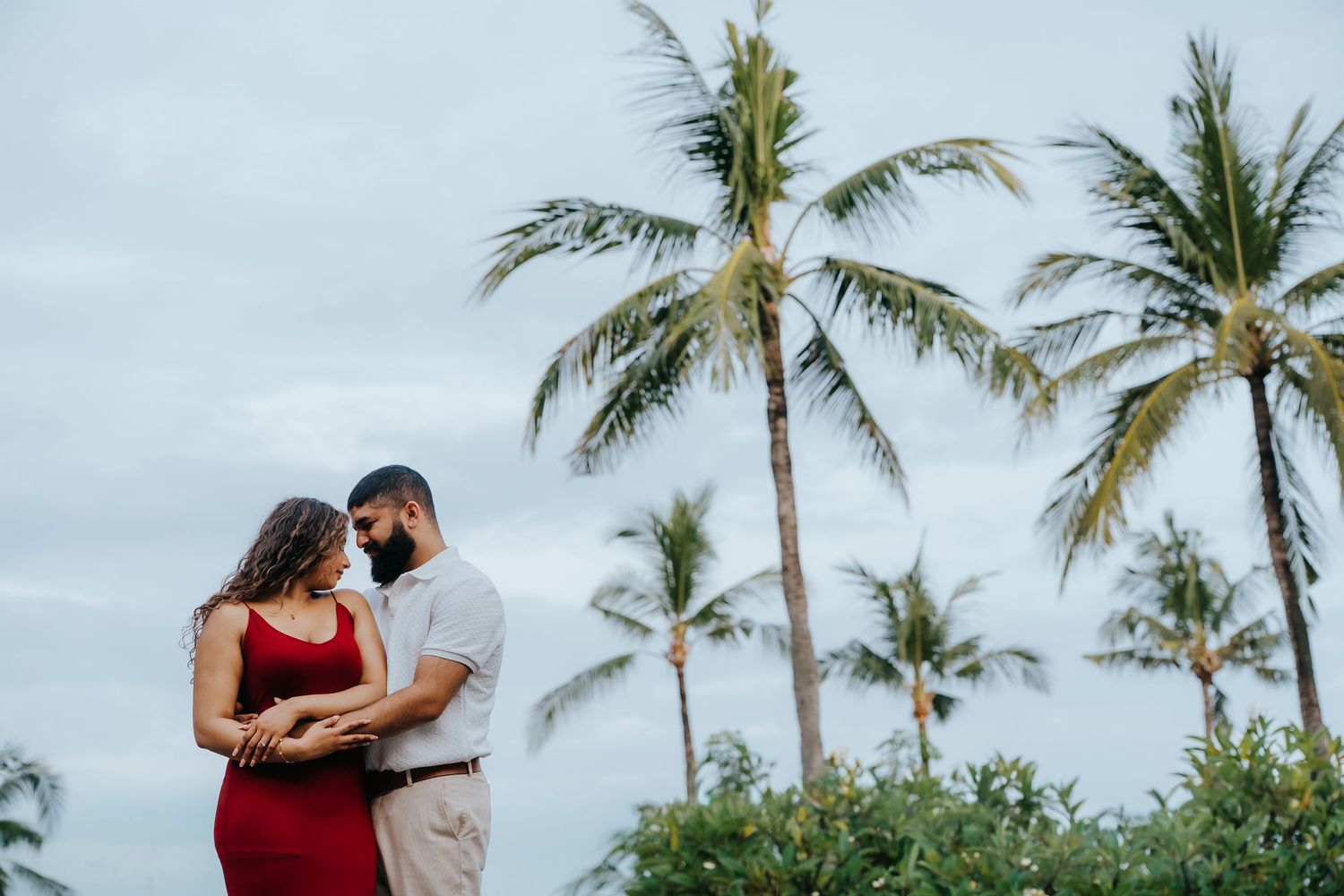 Palm trees sway against cloudy tropical sky during beach photoshoot.
