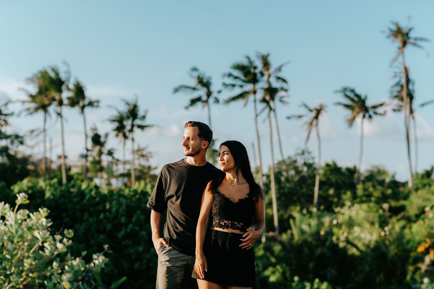 Palm trees line a tropical beach where a couple shares an intimate moment at sunset.