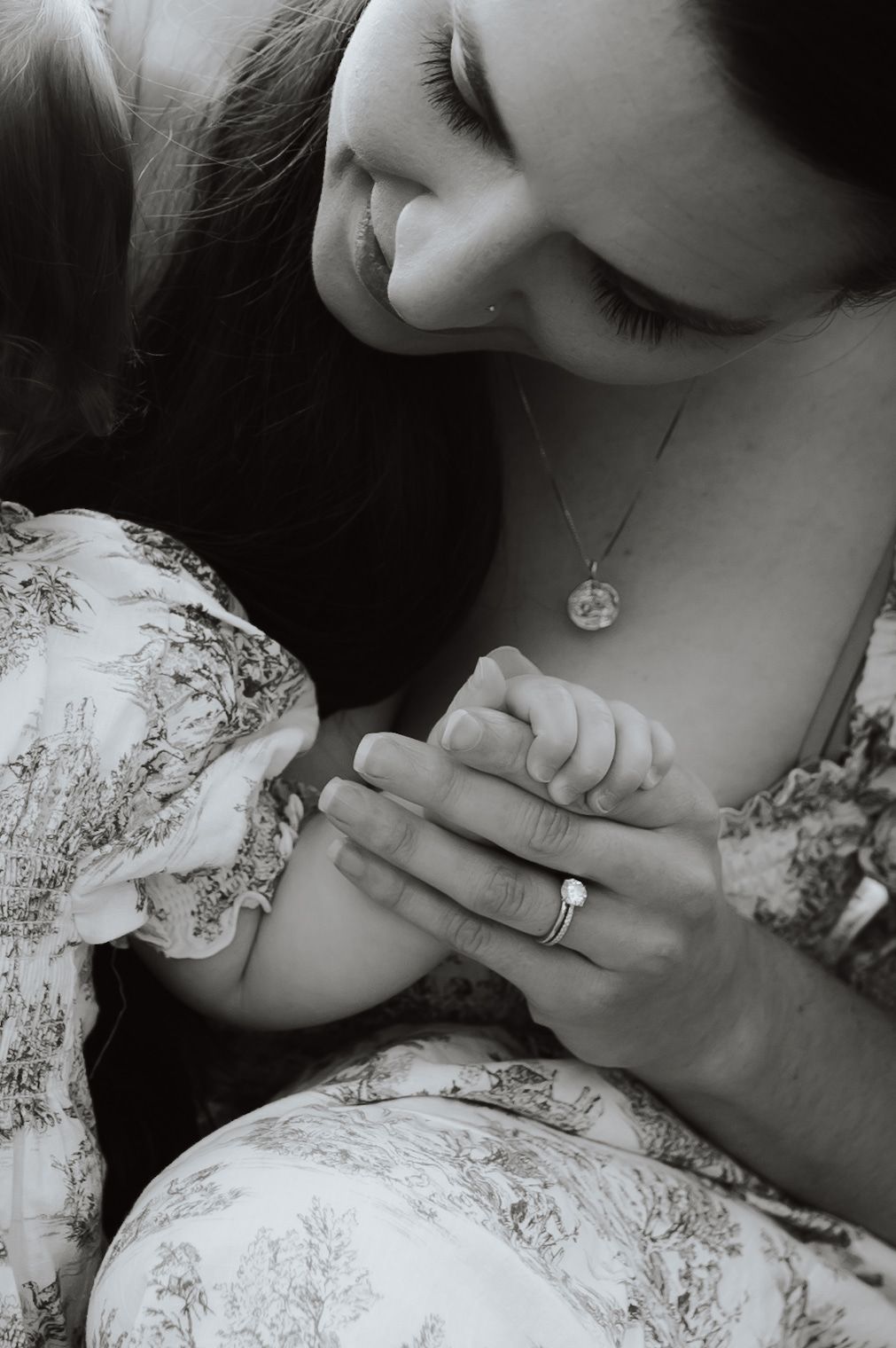 Black and white close-up photograph showing tender moment between parent and child in patterned clothing with jewelry.