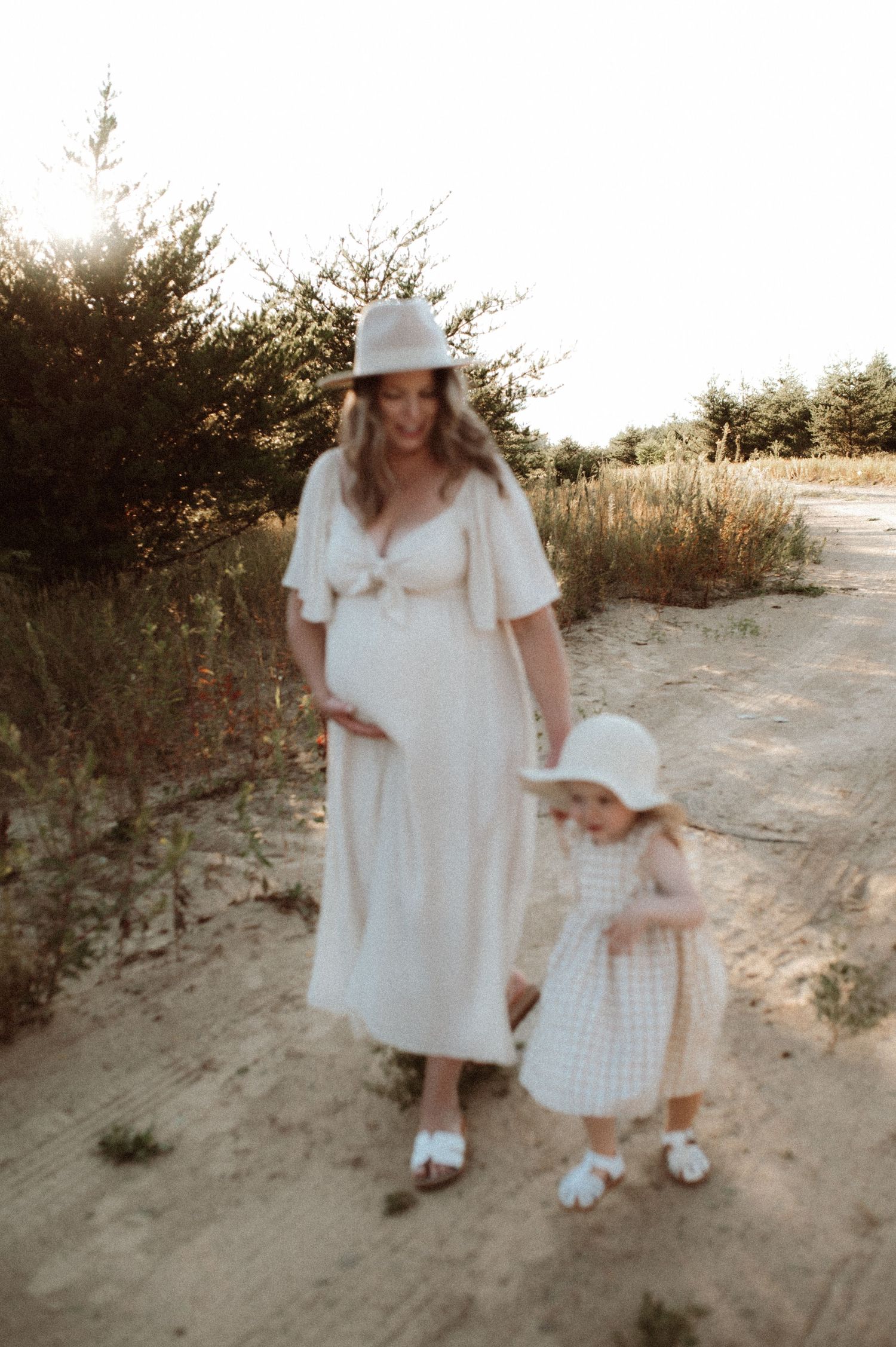 A pair of figures in white outfits walk hand-in-hand along a sandy beach path at sunset.