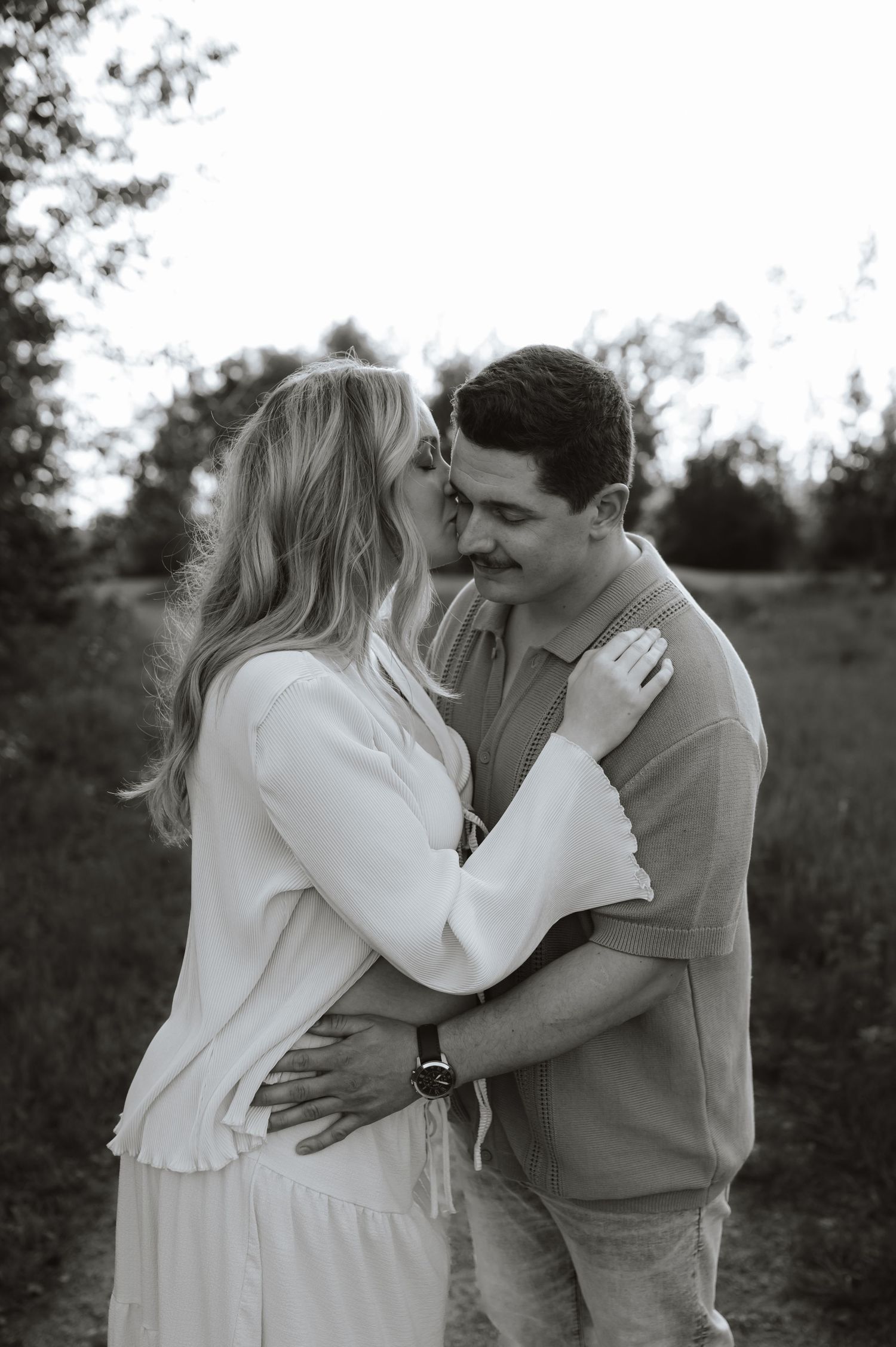 A romantic couple embracing in a natural outdoor setting, sharing tender moments in black and white photography.