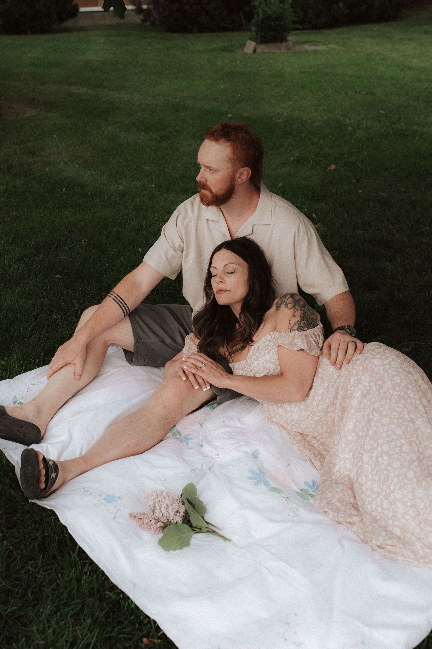 Couple lying together on a white blanket in the grass having an intimate outdoor photo session.