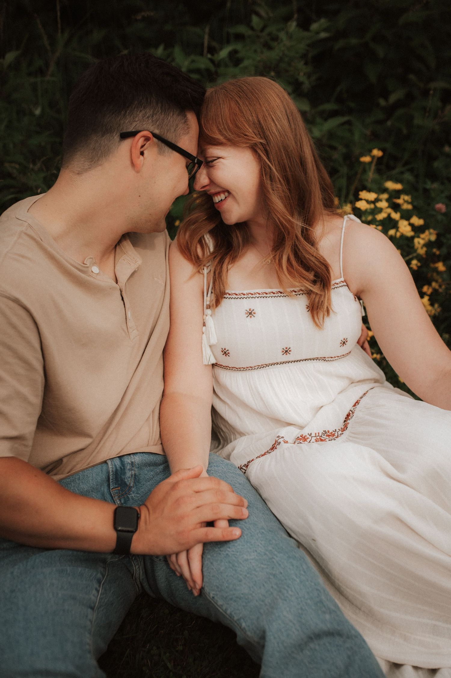 A romantic couple in casual beige and white clothing share an intimate moment outdoors among yellow flowers.