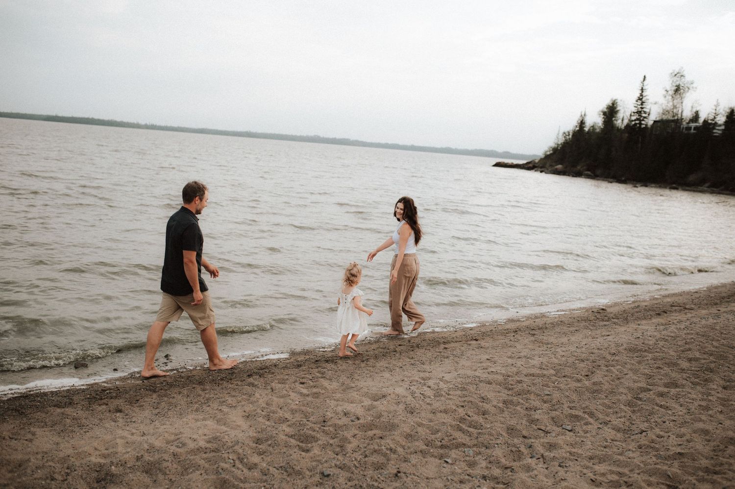A couple stands at the water's edge of a misty beach during sunset.