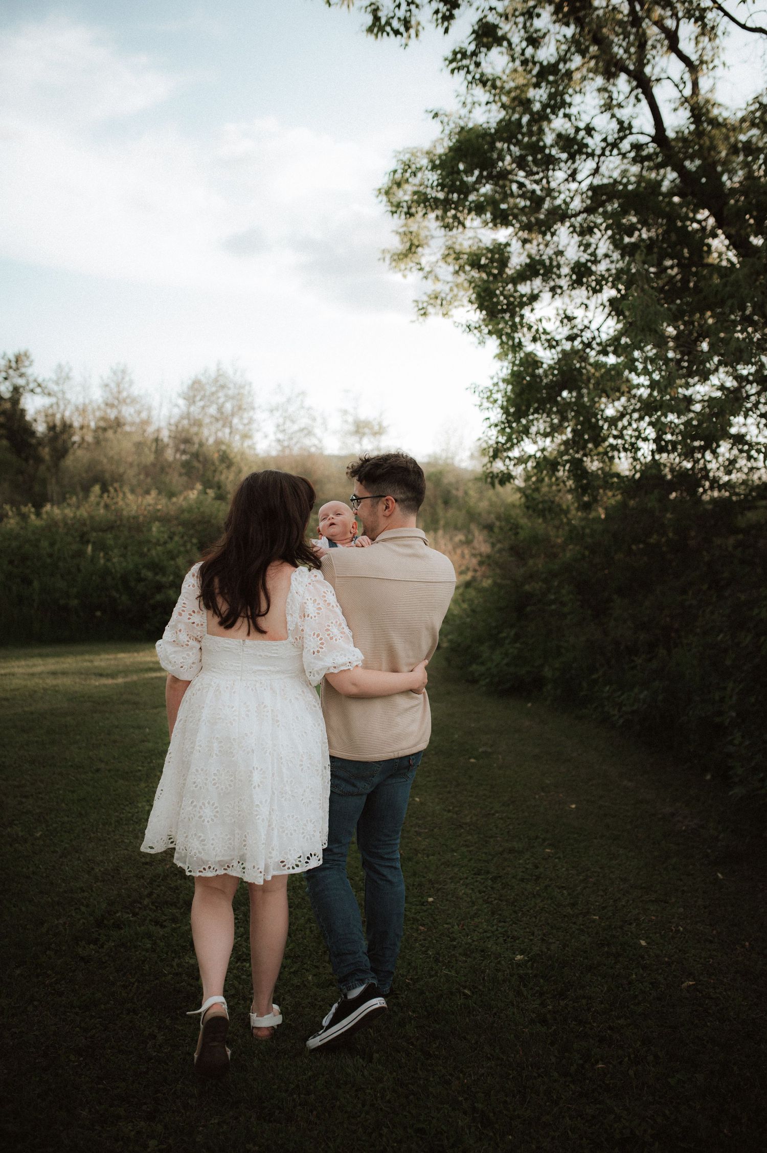 Couple walking together through a grassy field at sunset holding hands in a romantic outdoor setting.
