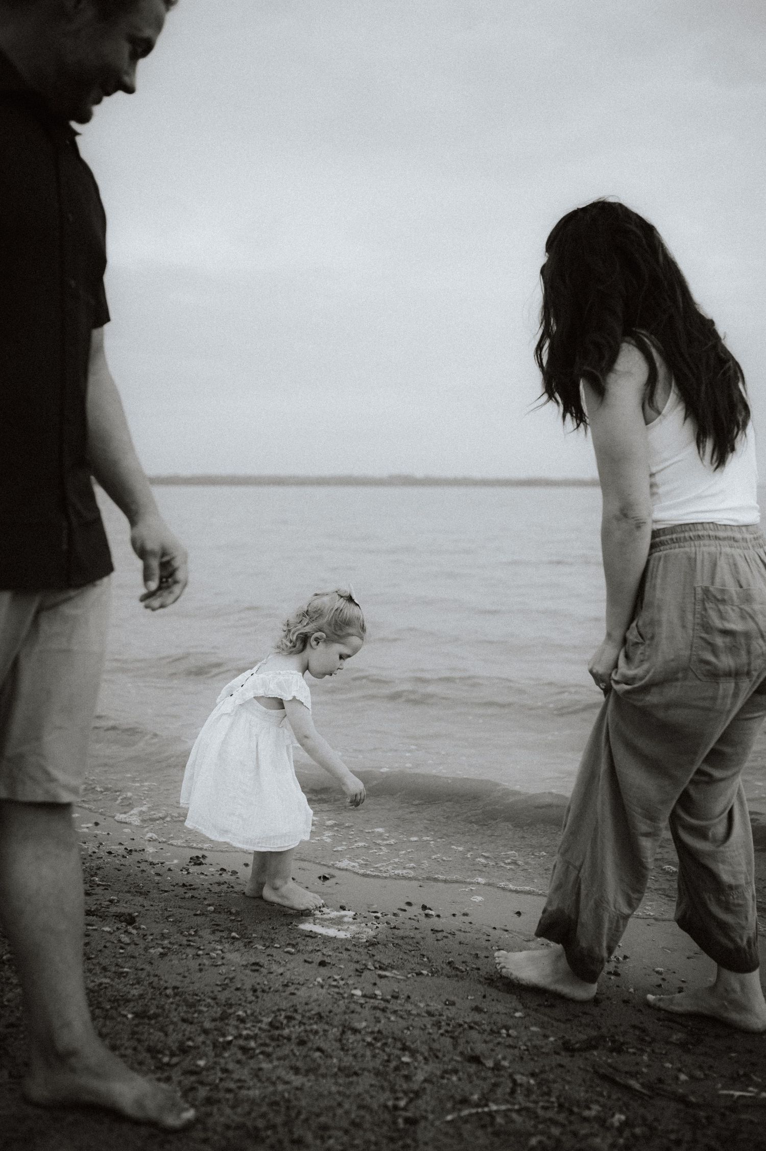 Family enjoying time with toddler at the beach in black and white.