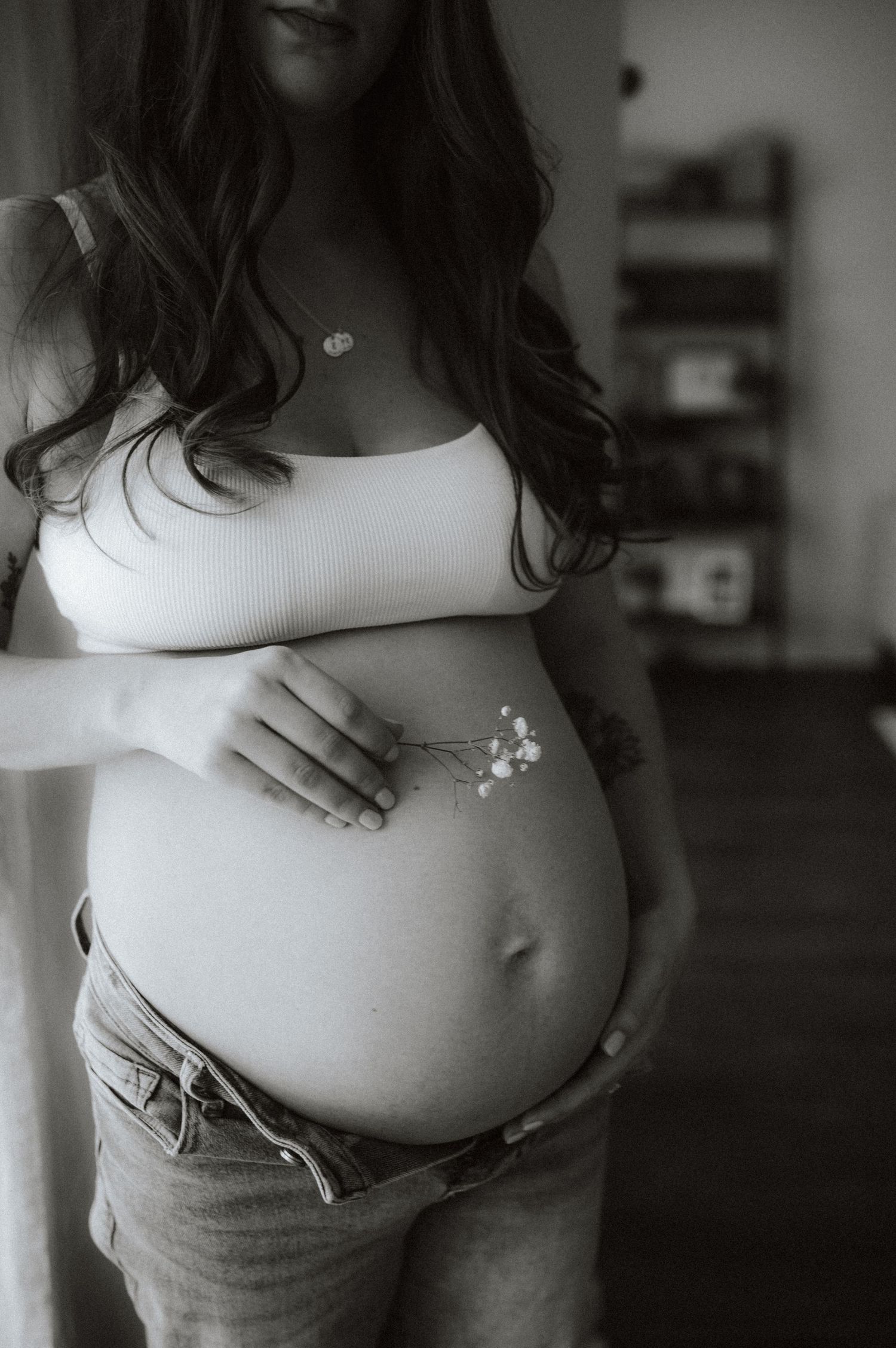 Black and white maternity photo showing pregnant belly with a delicate necklace and white tank top.