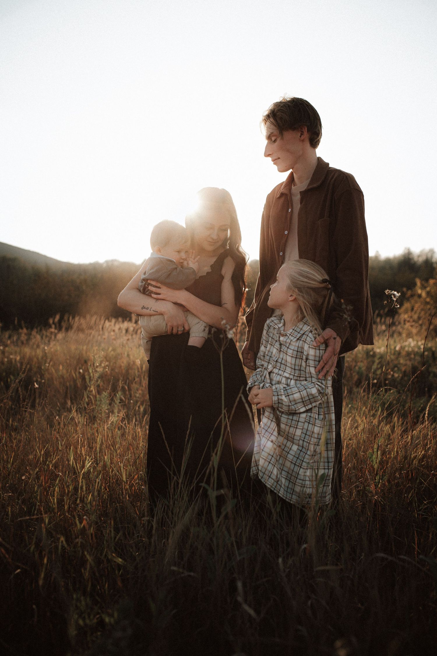 Family stands together in golden sunlit field during sunset creating a warm silhouette against the glowing sky.