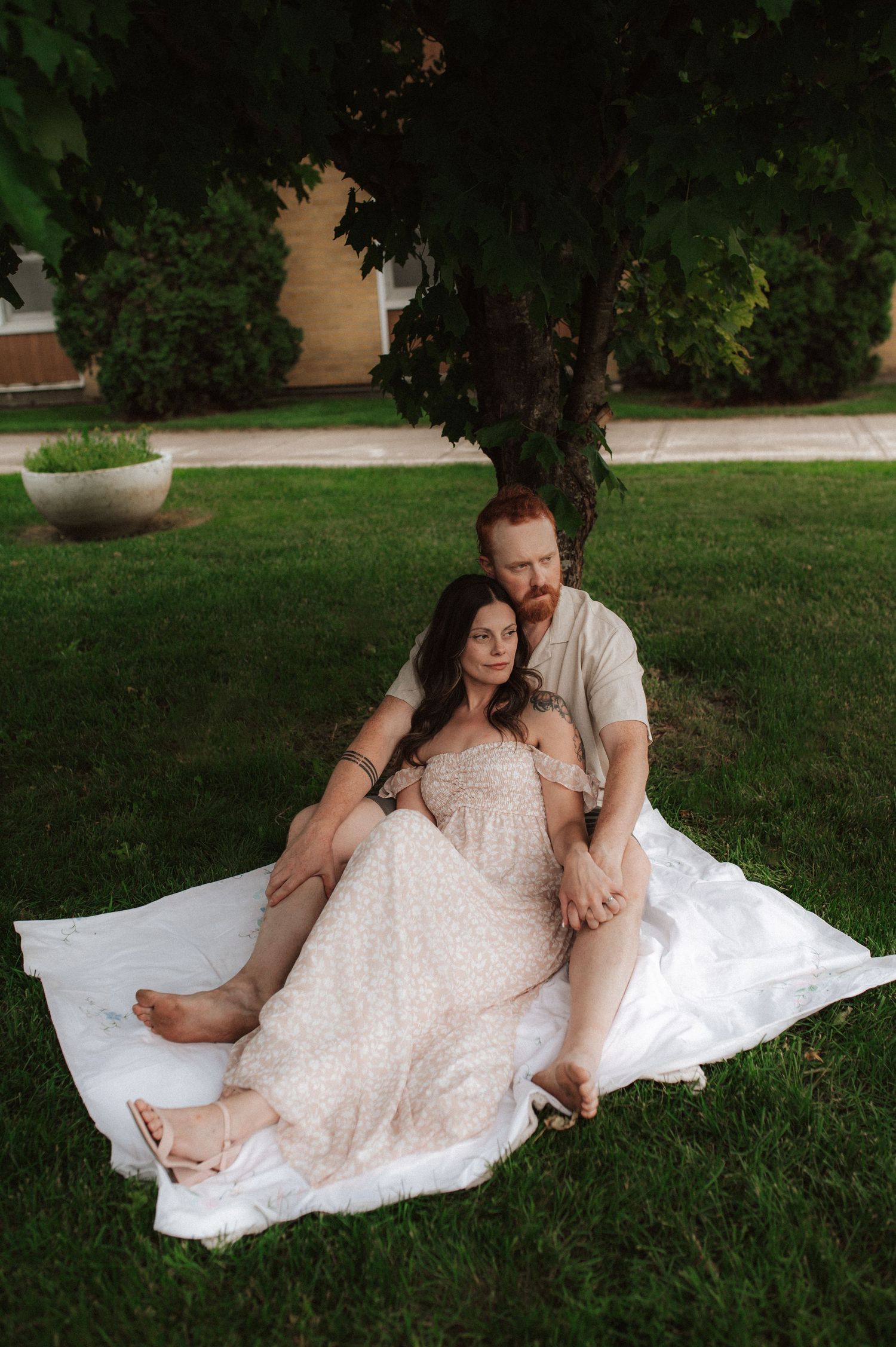 A romantic couple relaxes together on a white blanket in the grass during an outdoor photo session.