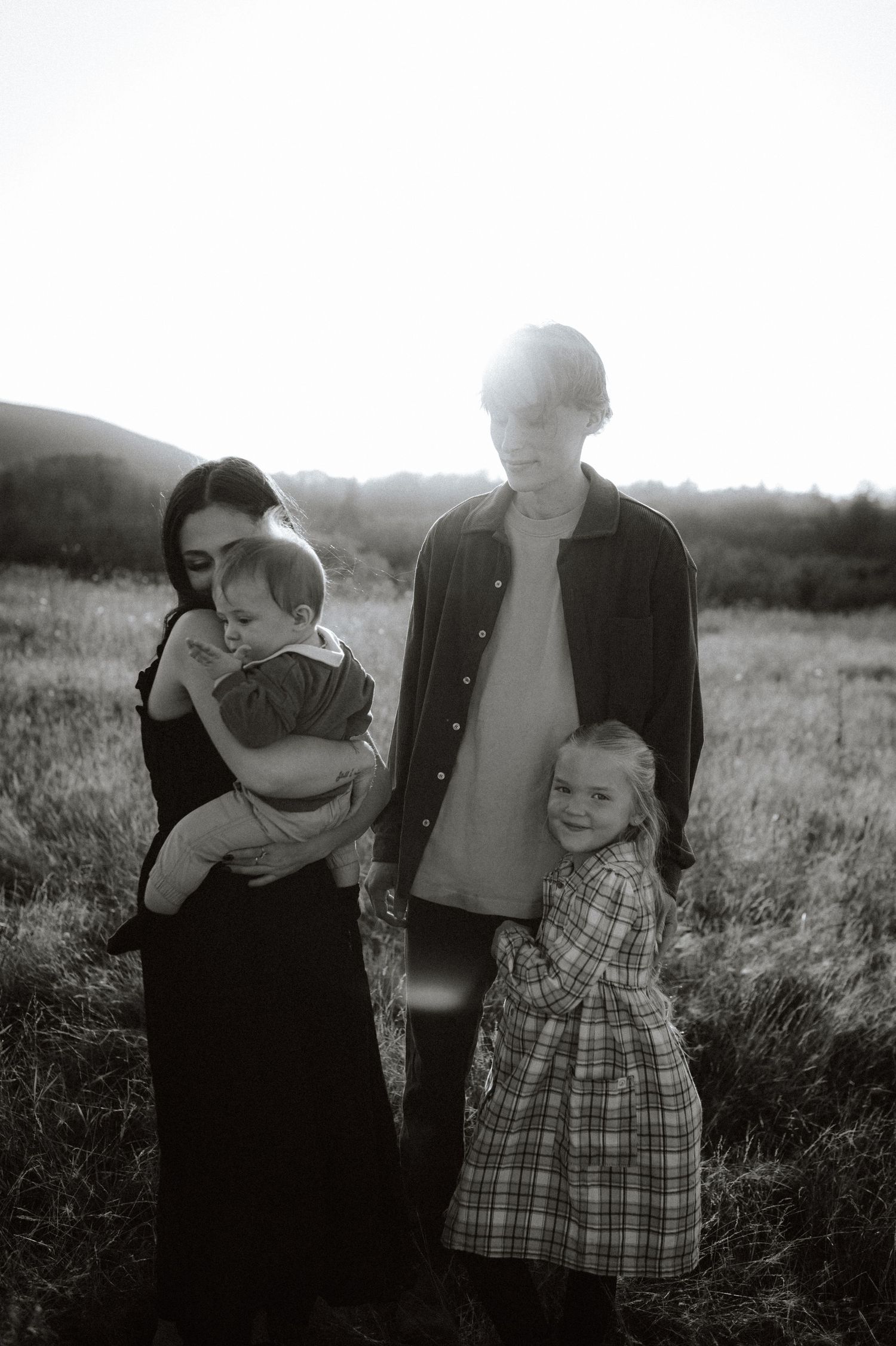 A black and white candid series of family photos captured in a grassy field during golden hour.