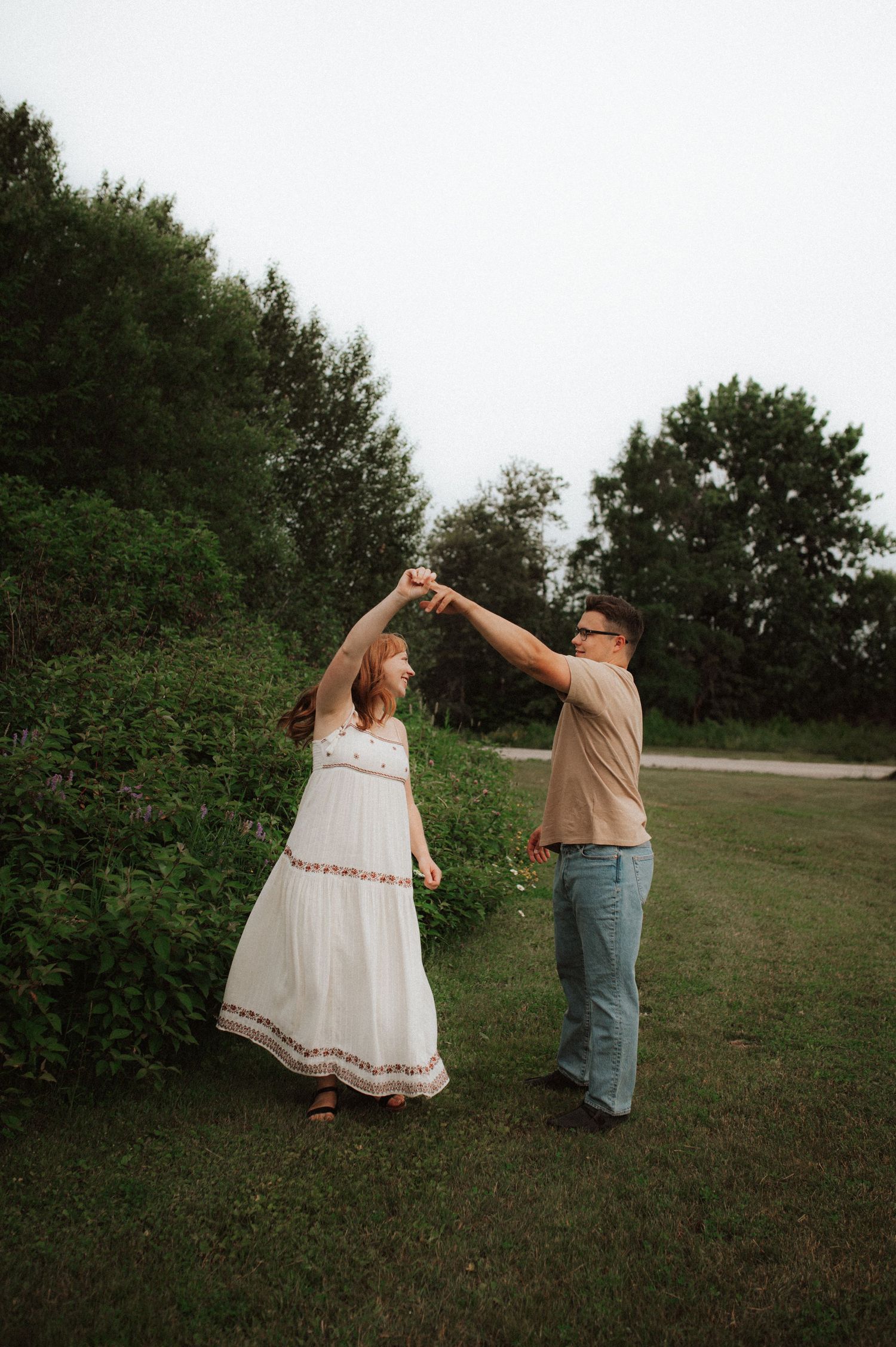 A couple dancing together on a grassy lawn with trees in the background during a romantic outdoor moment.