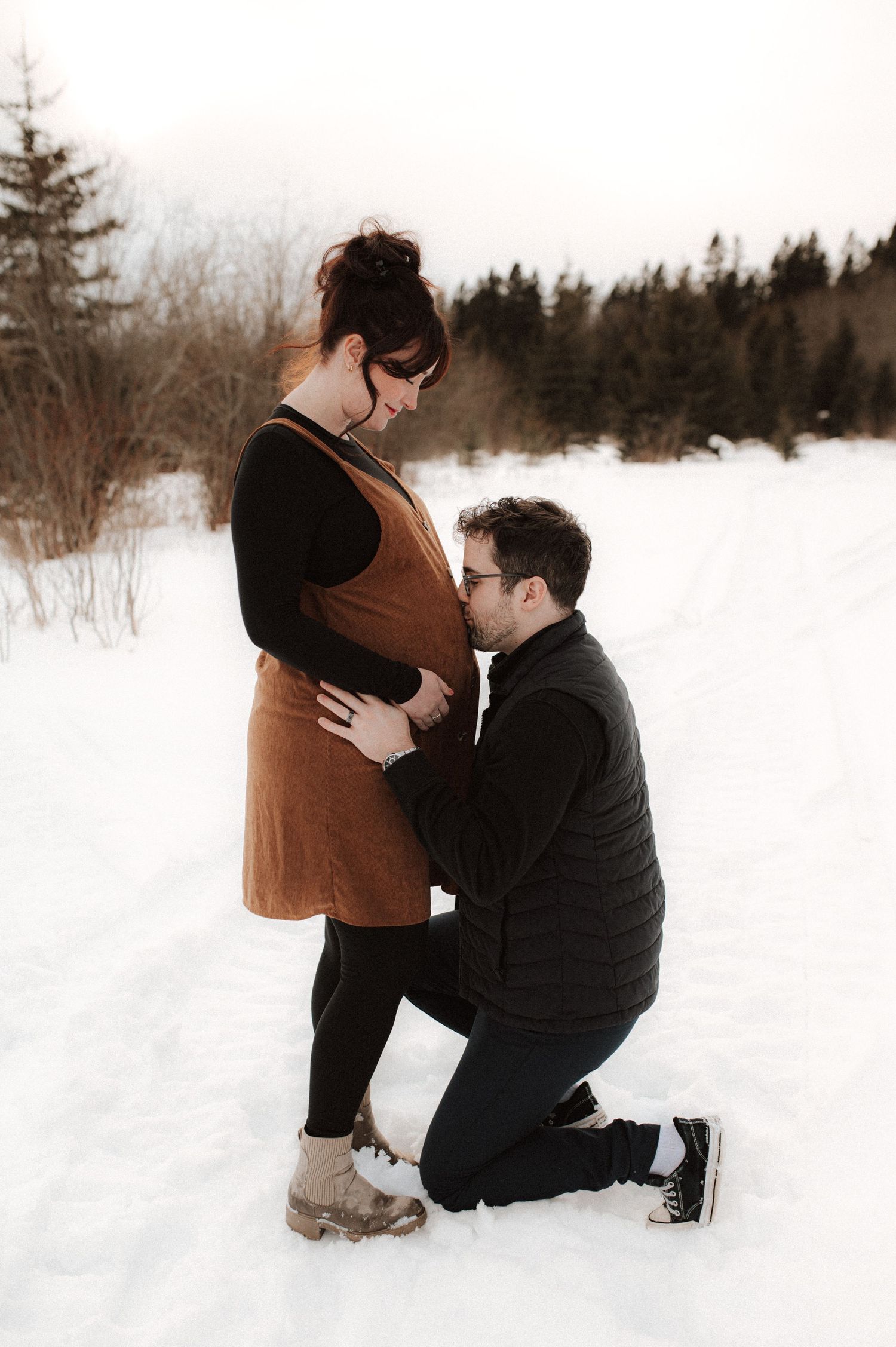 A heartwarming winter maternity photo shoot shows a couple sharing tender moments in a snowy landscape.