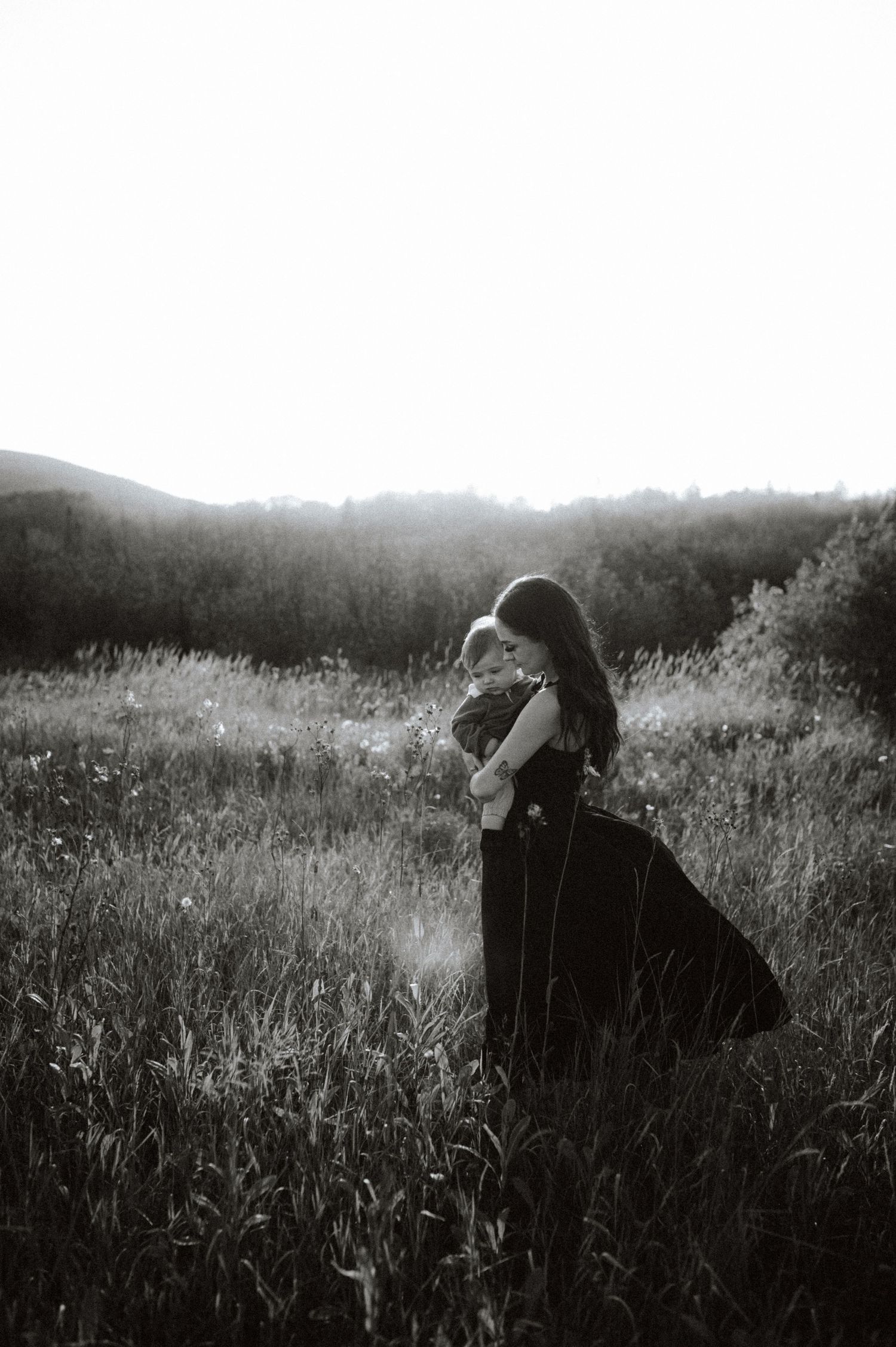 Person gazes into distance while laying in tall grass field captured in dramatic black and white photography series.