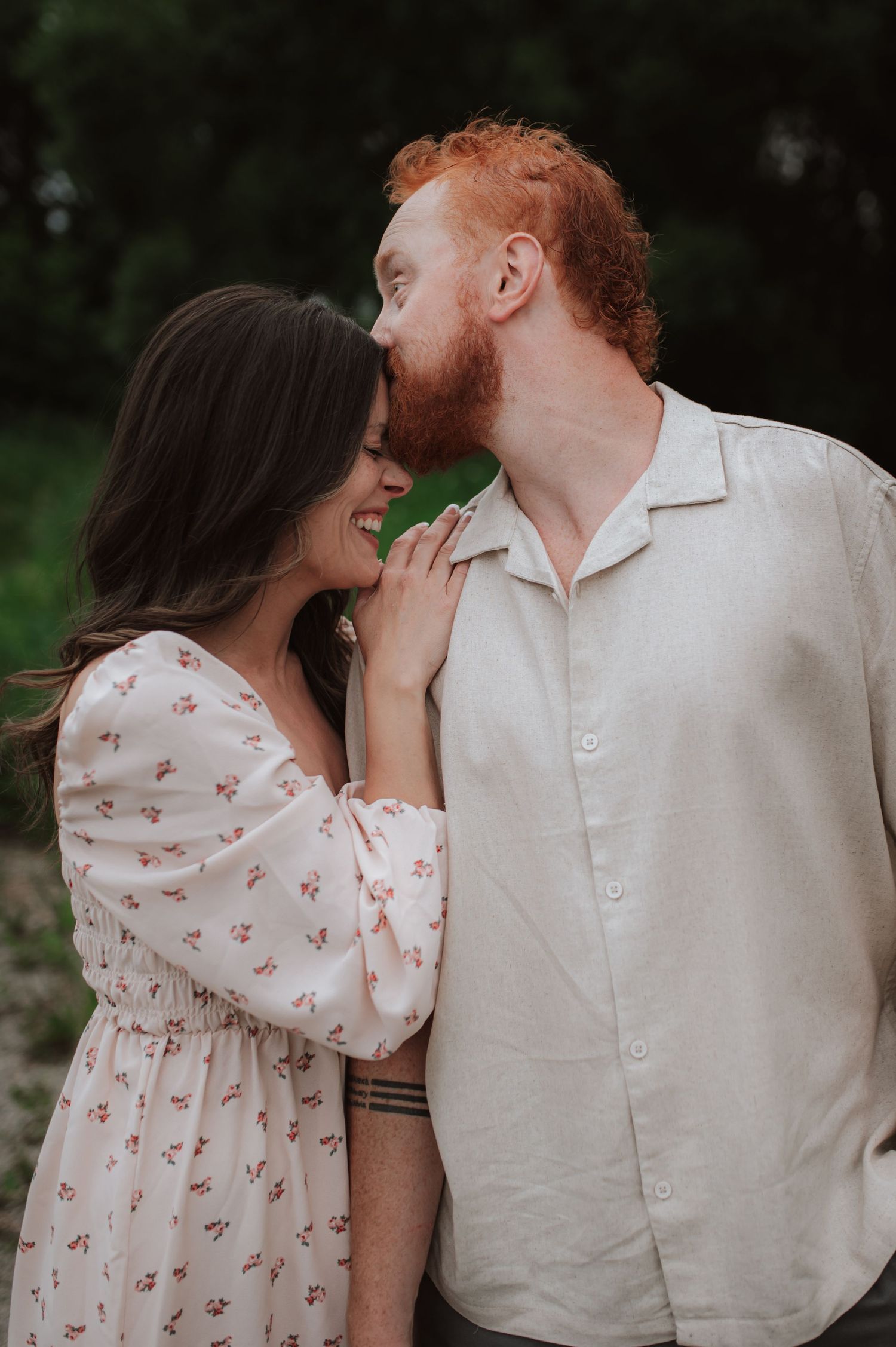A romantic outdoor couple photo showing sweet affection between partners in coordinated white and pink outfits.