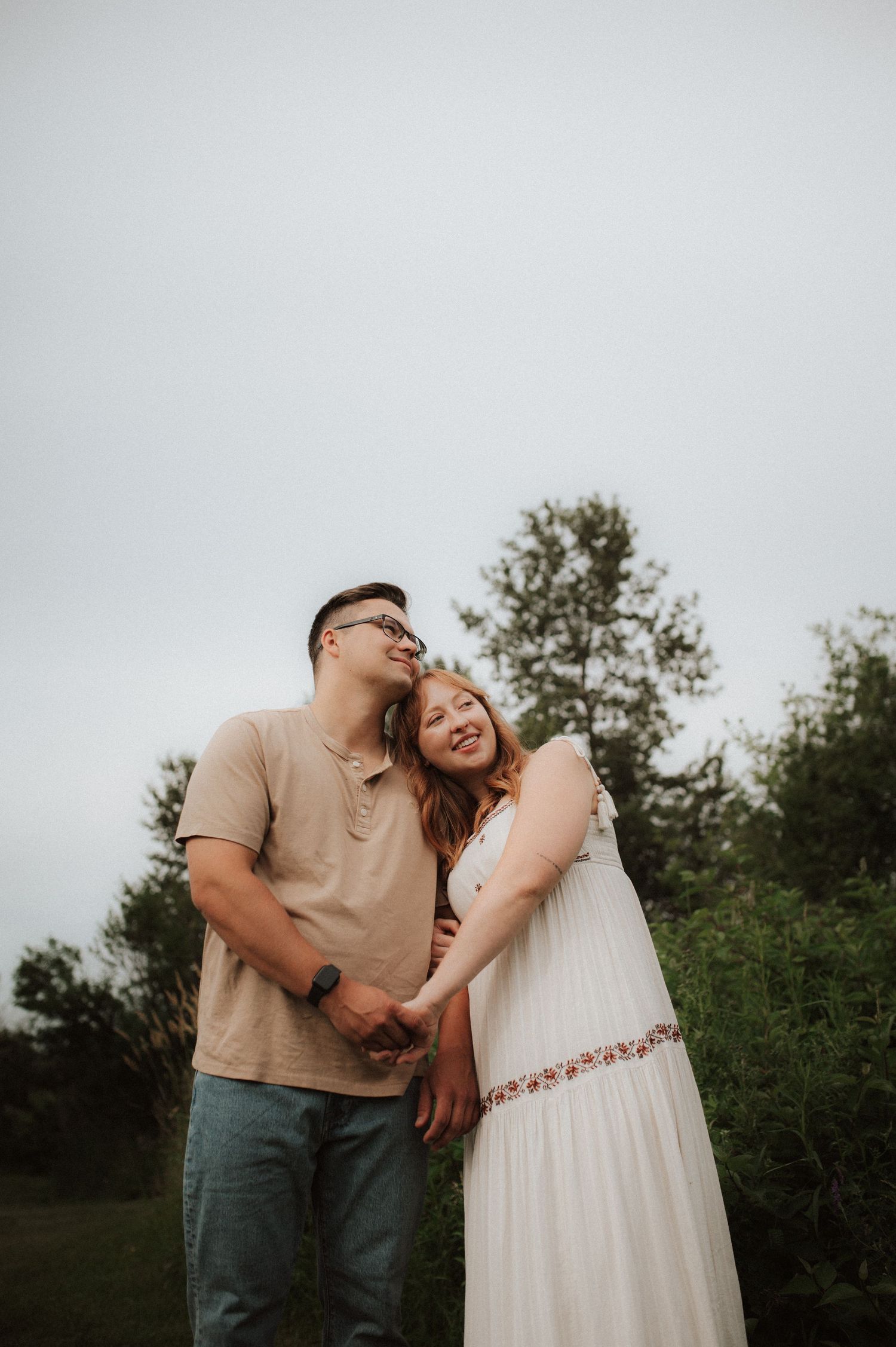A couple shares joyful laughter and tender moments in a romantic outdoor photoshoot against green foliage.