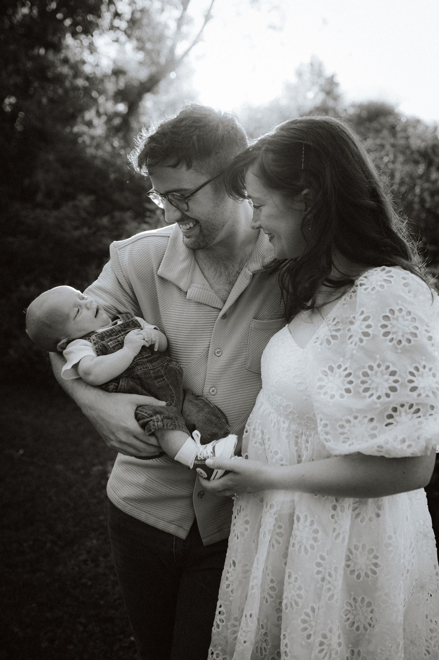 A black and white photo series showing a tender moment between two parents and their newborn baby outdoors.