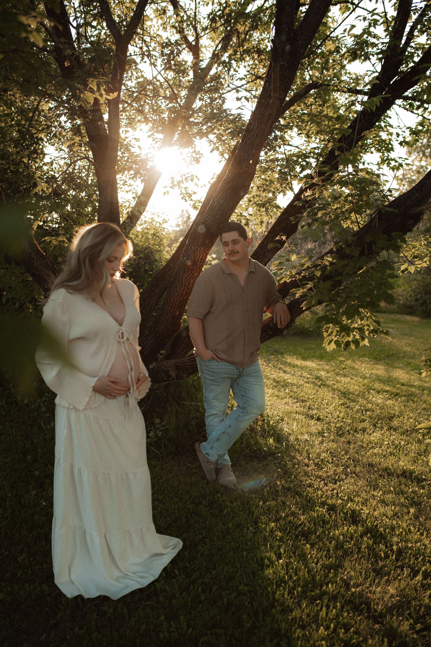 Sun peeks through trees as figures stand together in tall grass at golden hour creating a warm natural silhouette.