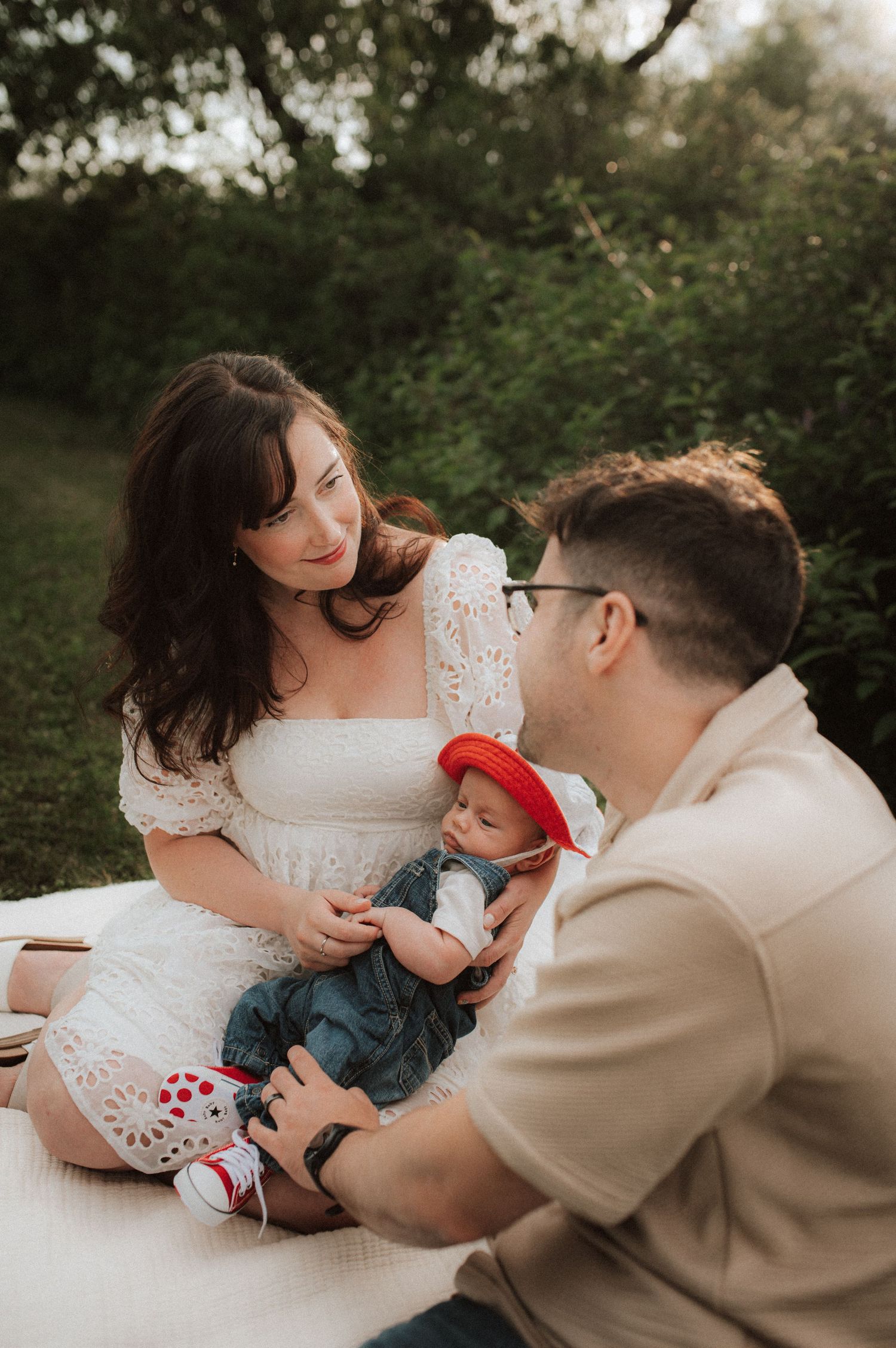 Intimate family moment on a white blanket surrounded by lush greenery during an outdoor photo session.