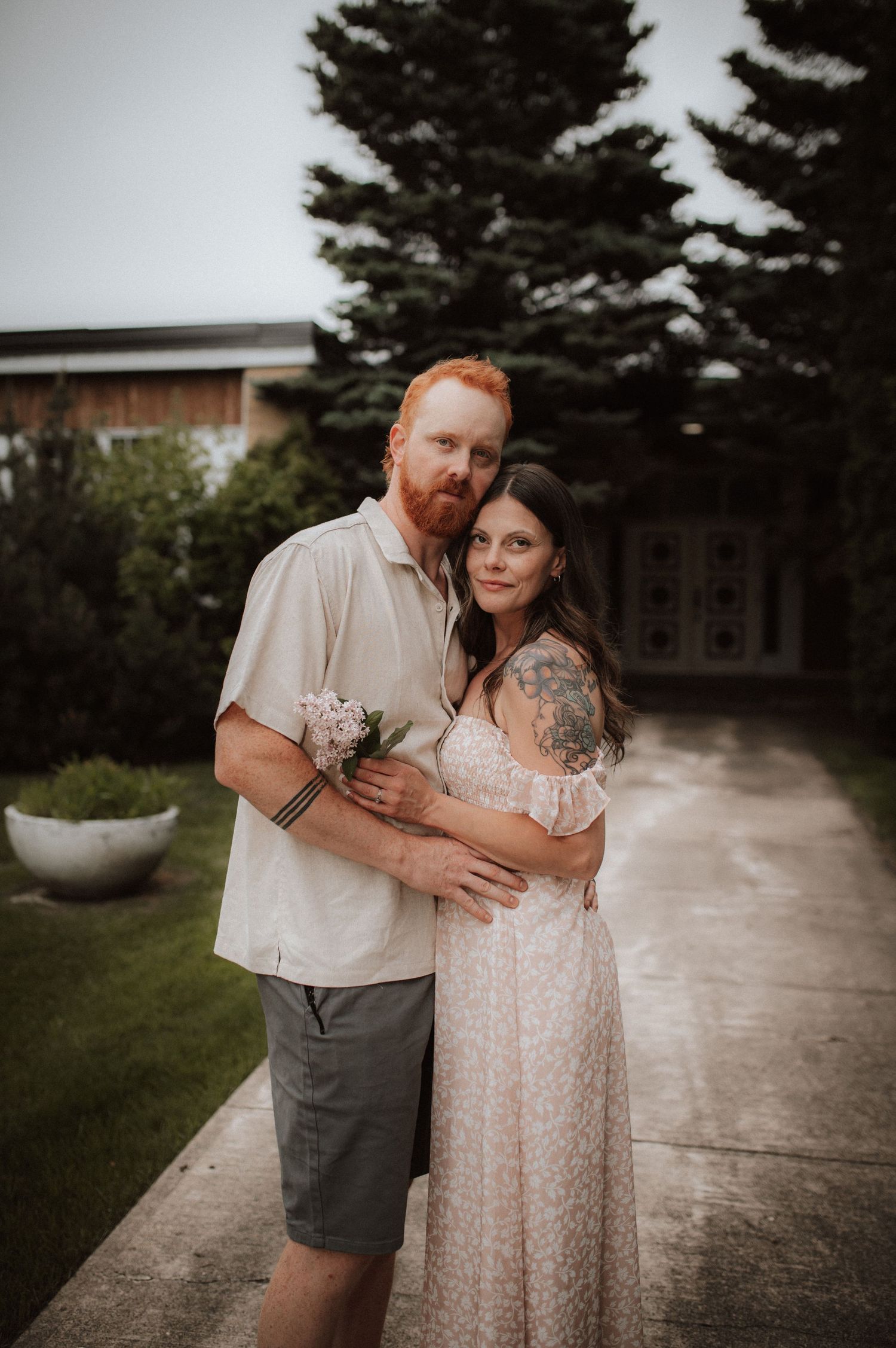 A romantic couple shares intimate moments in a garden setting wearing light summer attire and holding delicate flowers.