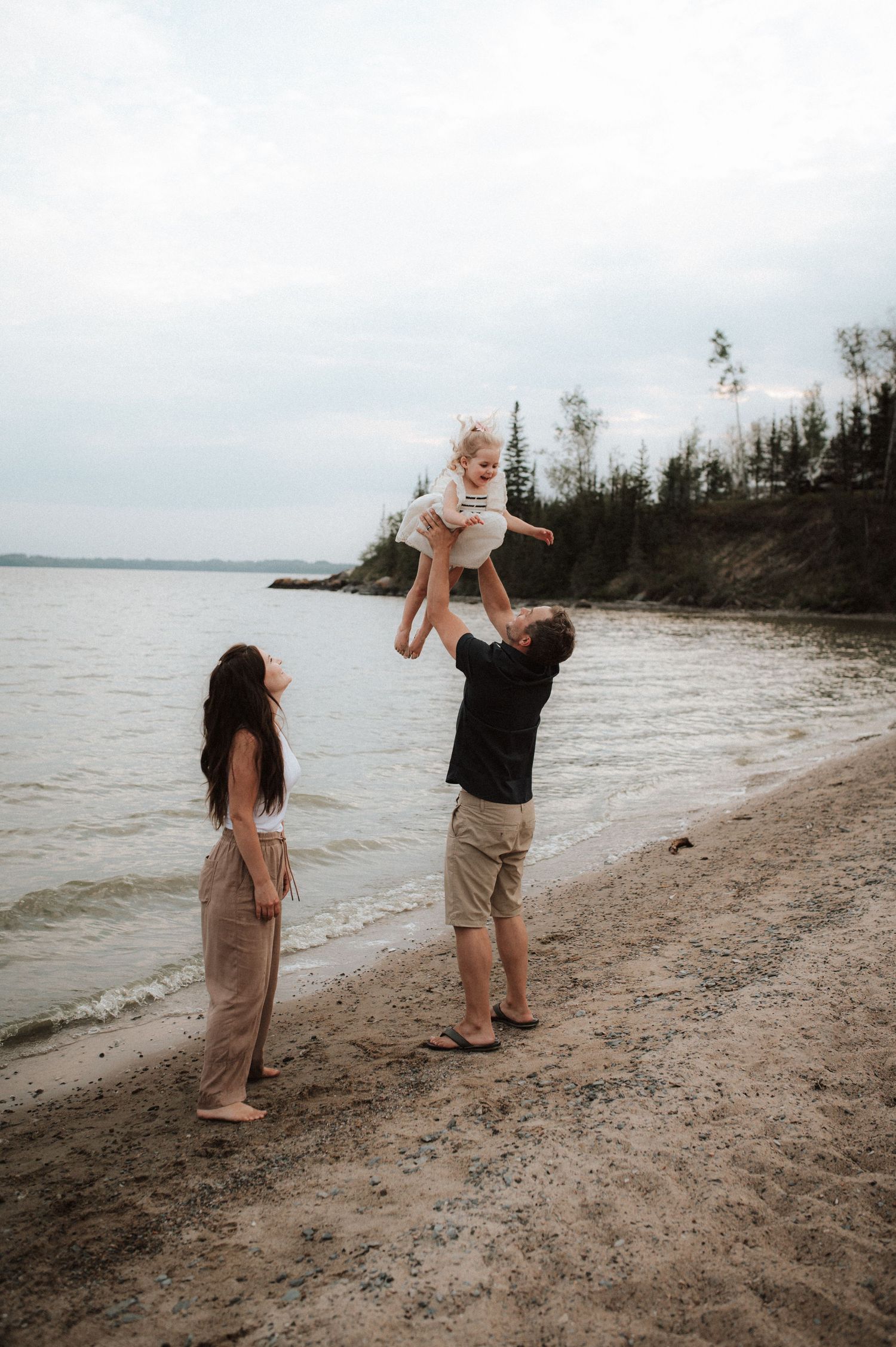 A family shares a joyful moment together on a scenic beach with trees and water in the background.