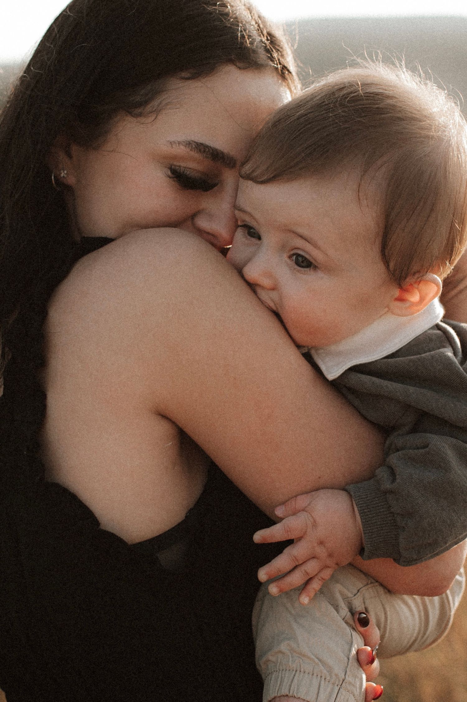 A tender motherly embrace and gentle kiss moment with a baby in a soft, warm-toned intimate portrait.
