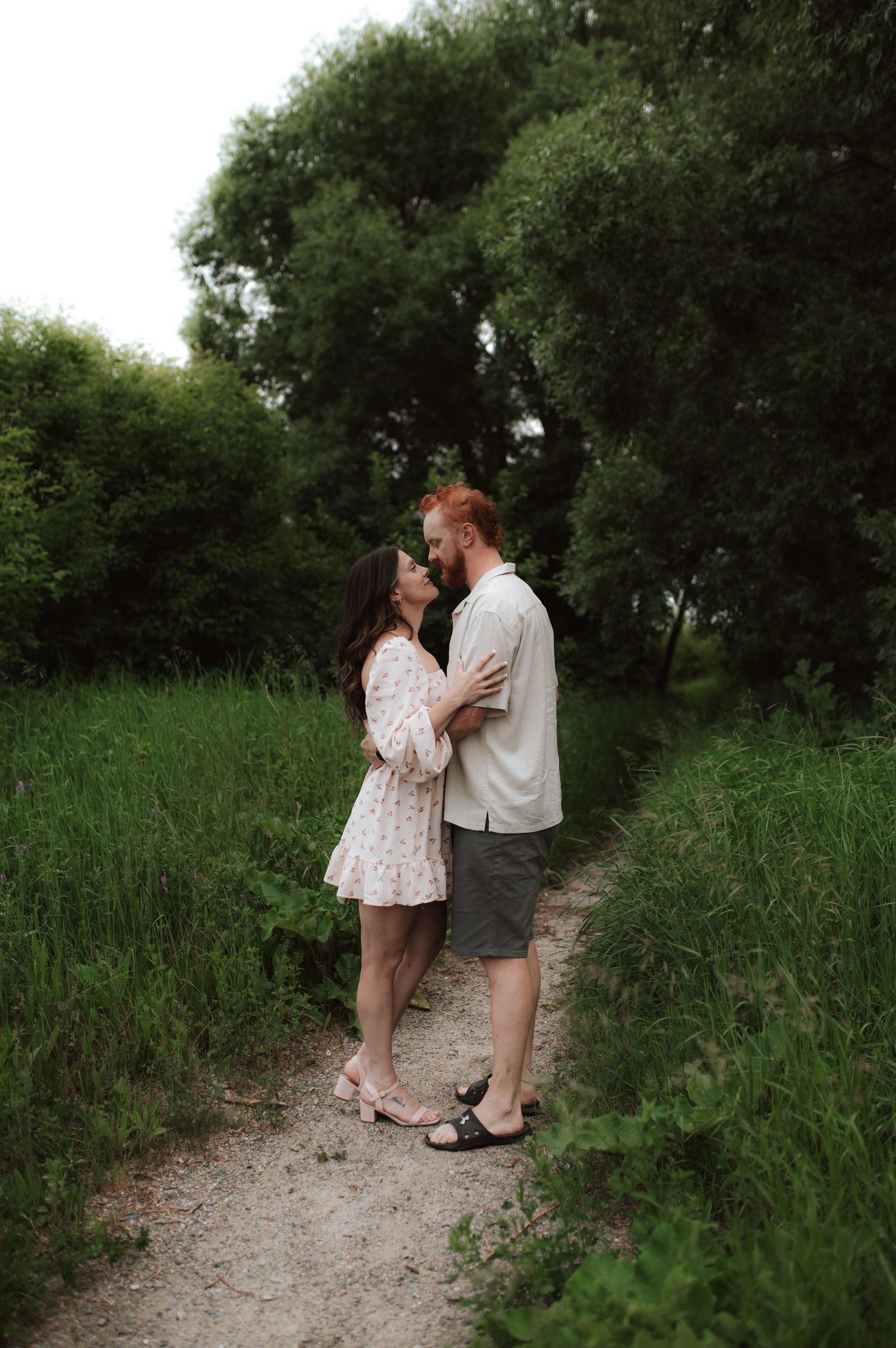 A couple shares a romantic moment together on a nature trail surrounded by lush green vegetation and trees.