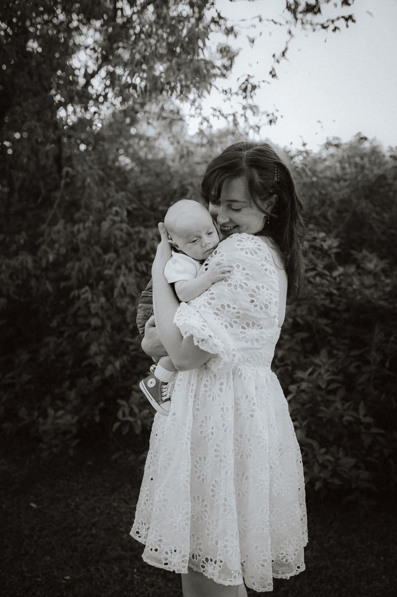 Two figures in flowing white eyelet lace dresses dance together in a dreamy black and white outdoor scene.